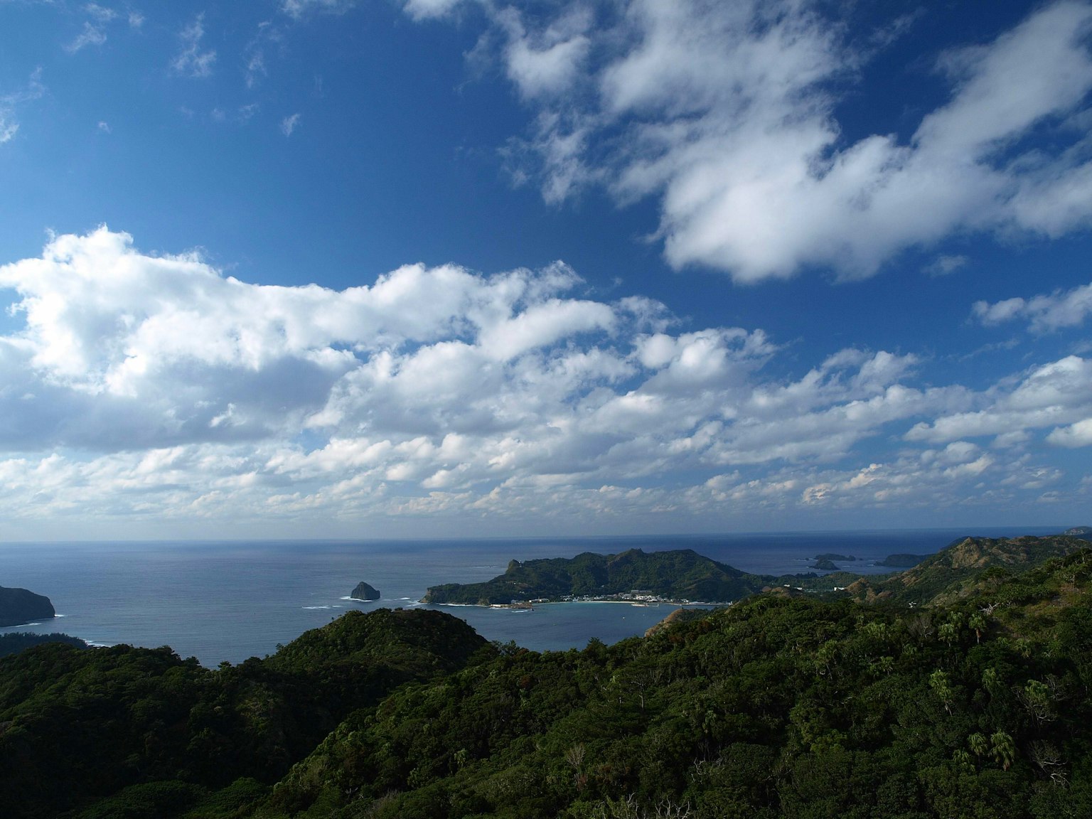 Vista panoramica di colline verdi e oceano sotto un cielo blu con nuvole bianche