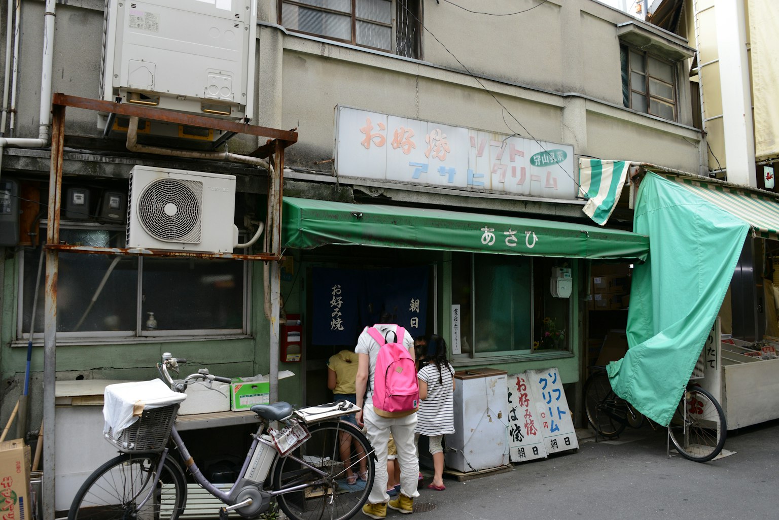 Außenansicht eines alten japanischen Geschäfts mit einem Kind und einem Erwachsenen, die vor einem geparkten Fahrrad stehen