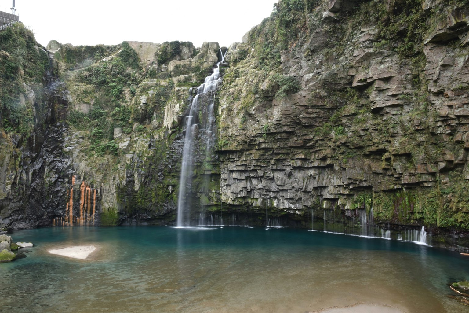 Una bellissima cascata che scende da scogliere lussureggianti in una piscina blu chiaro