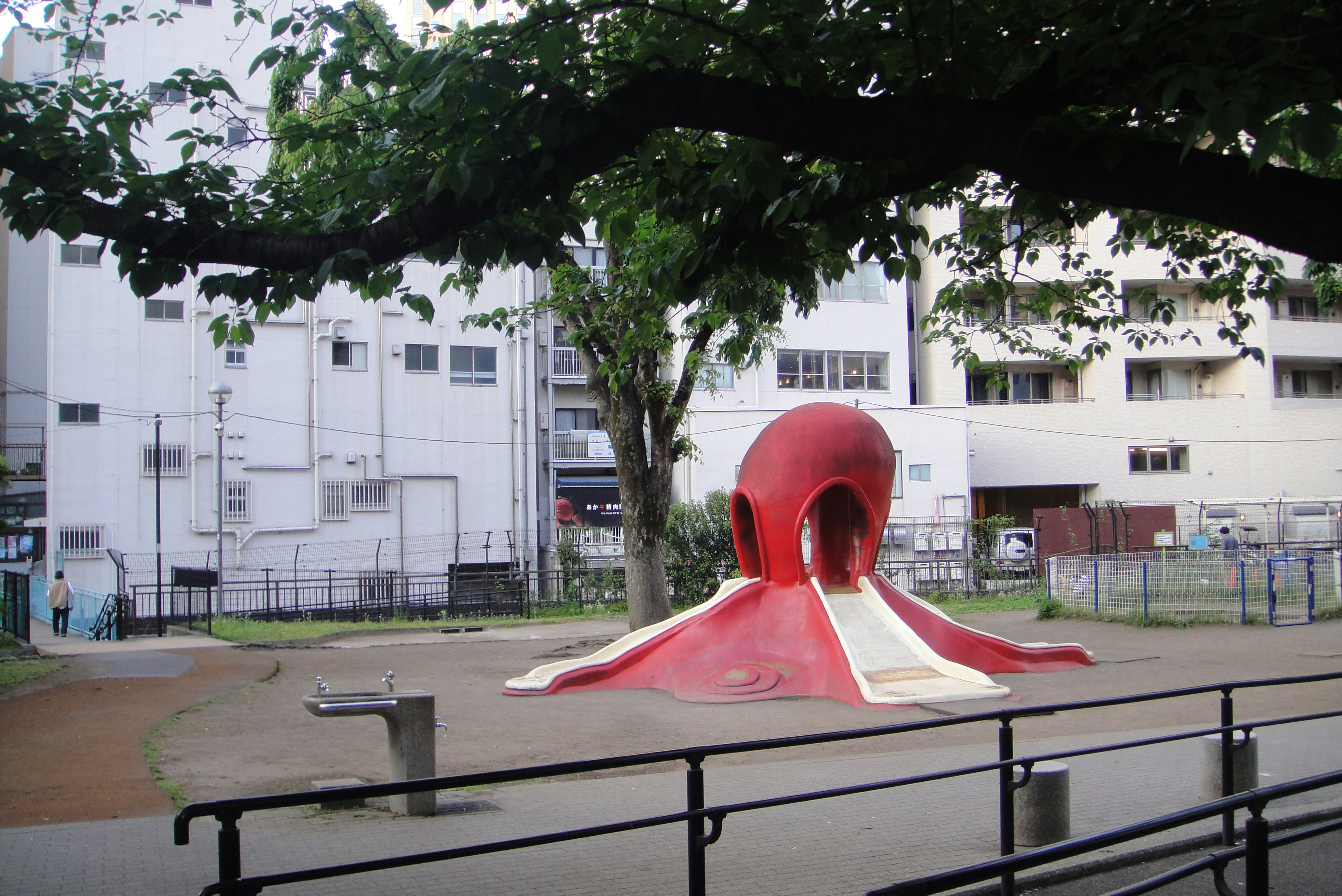 赤いタコのオブジェがある公園のベンチ前の広場