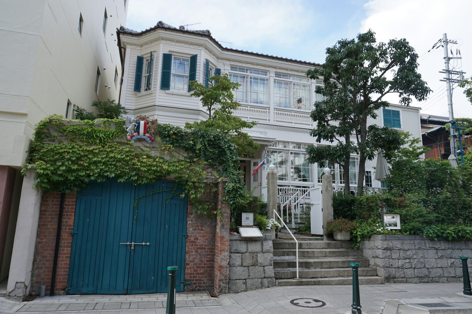 Hermosa casa con exterior blanco y persianas azules rodeada de vegetación y escaleras