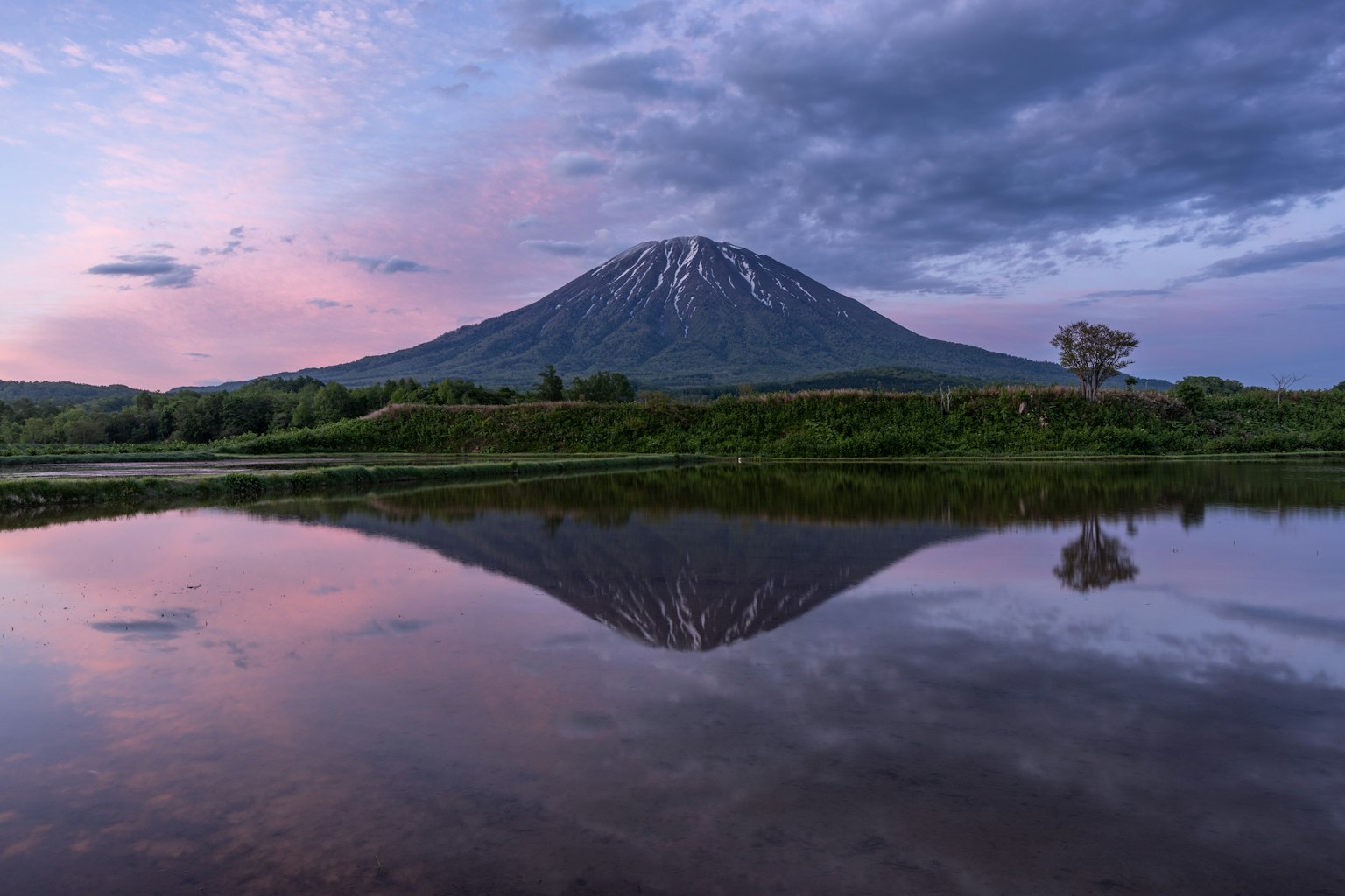 Ein ruhiger See, der einen schneebedeckten Berg unter einem bunten Sonnenuntergangshimmel spiegelt