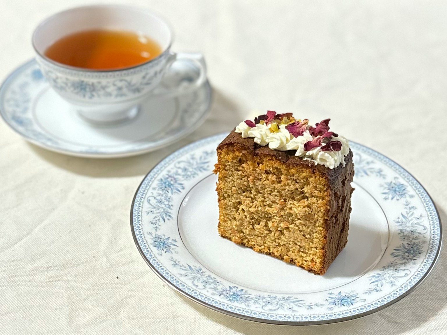 Una fetta di torta con crema e petali di rosa accanto a una tazza di tè