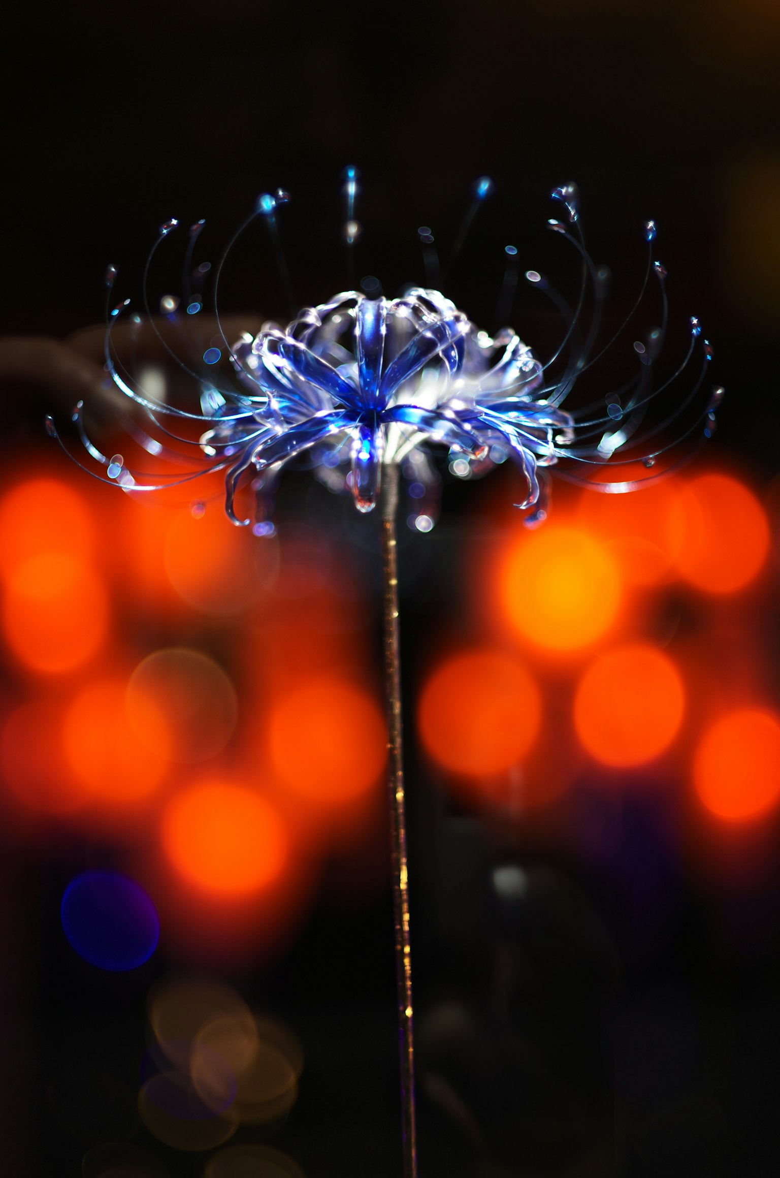Leuchtendes, blumenförmiges Objekt in Blau mit verschwommenem orangefarbenem Hintergrund