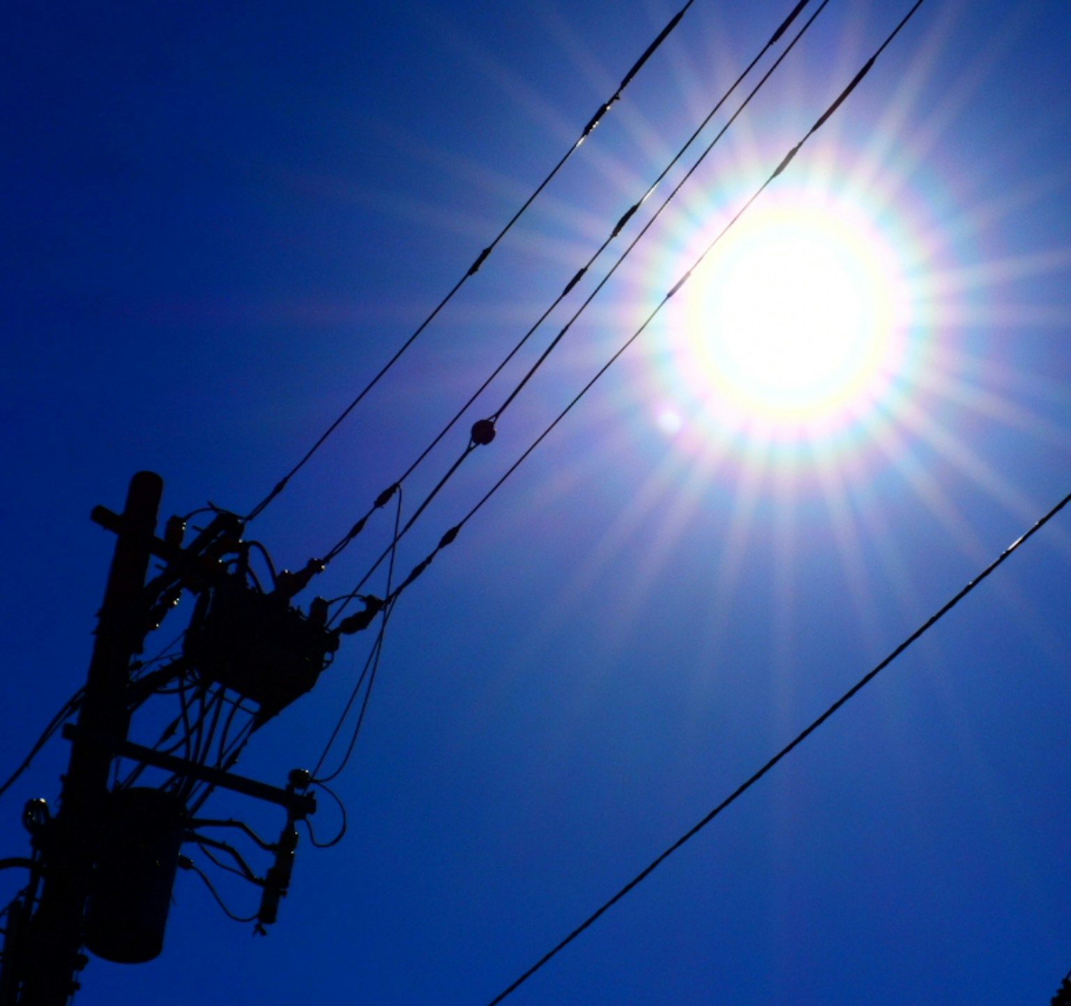 Silhouette di un palo elettrico sotto un sole brillante in un cielo blu