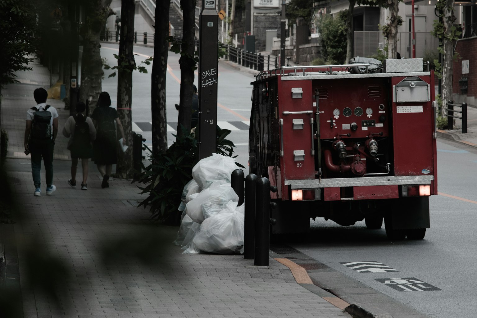 A red vehicle parked on the street with garbage bags nearby