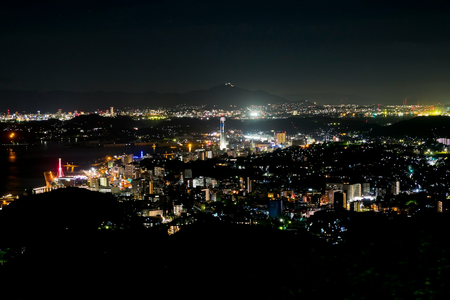 Night view of a city with illuminated buildings and Mount Fuji silhouette