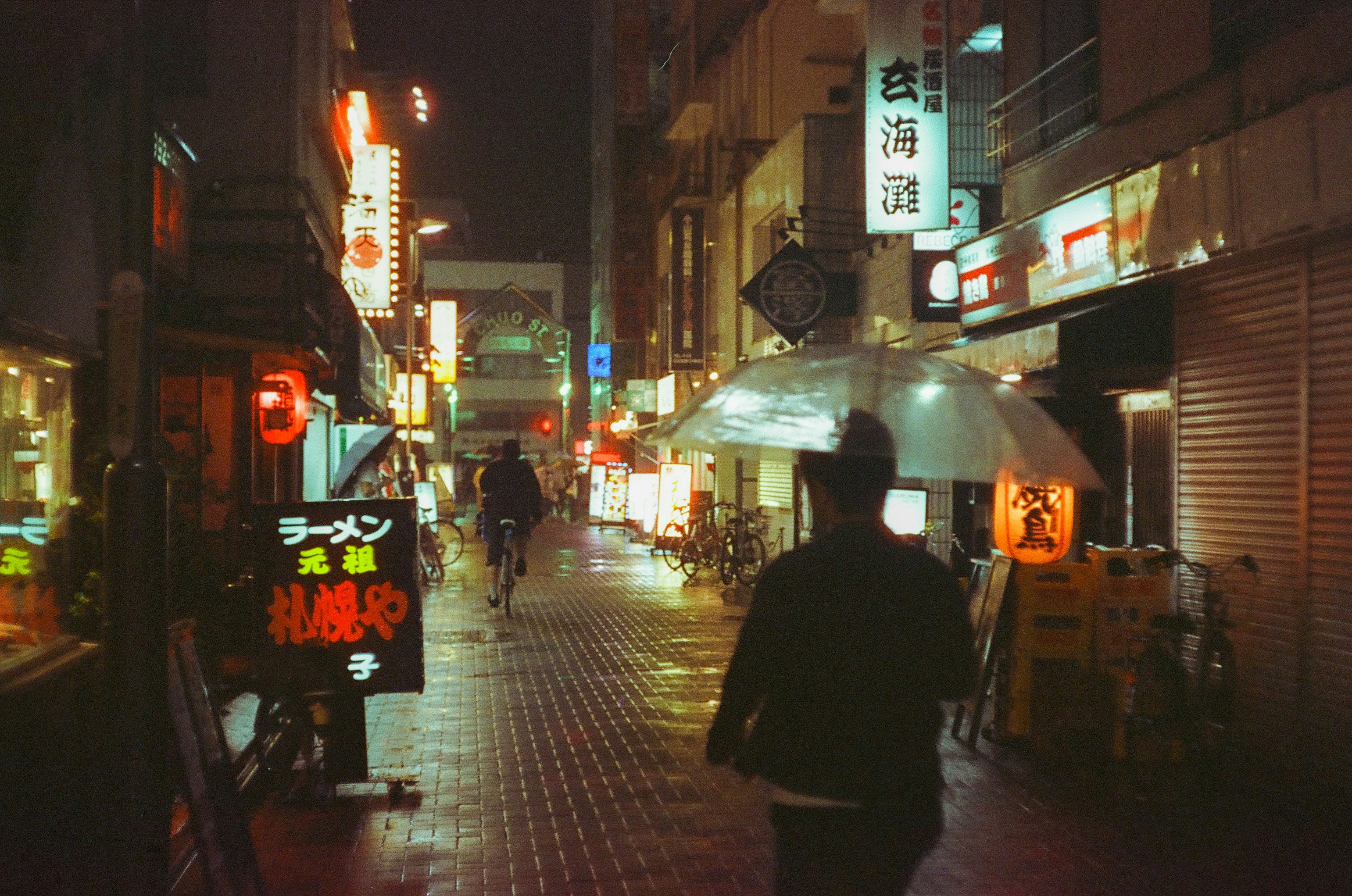 雨の路地に並ぶ提灯と看板のある飲食店街