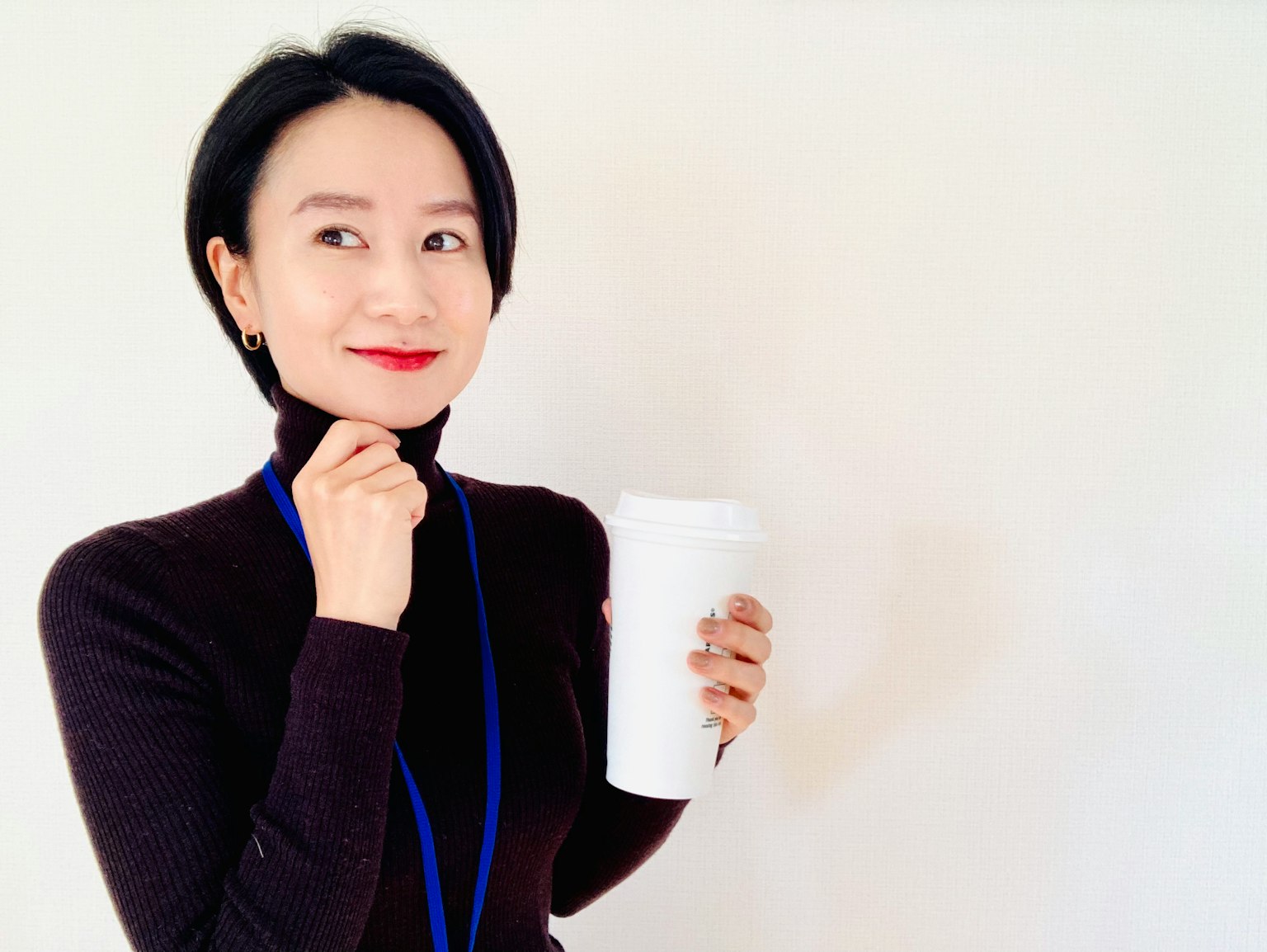 穿著黑色高領衫的女性手持白色杯子微笑