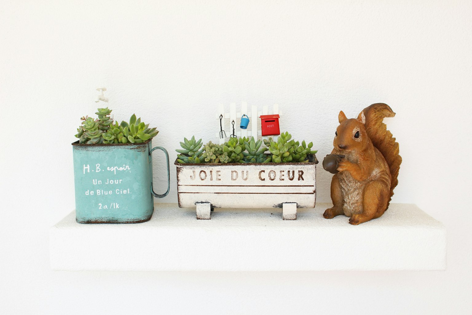 Mensola decorativa con succulente in un vaso blu e un vaso bianco con una statuetta di scoiattolo a destra