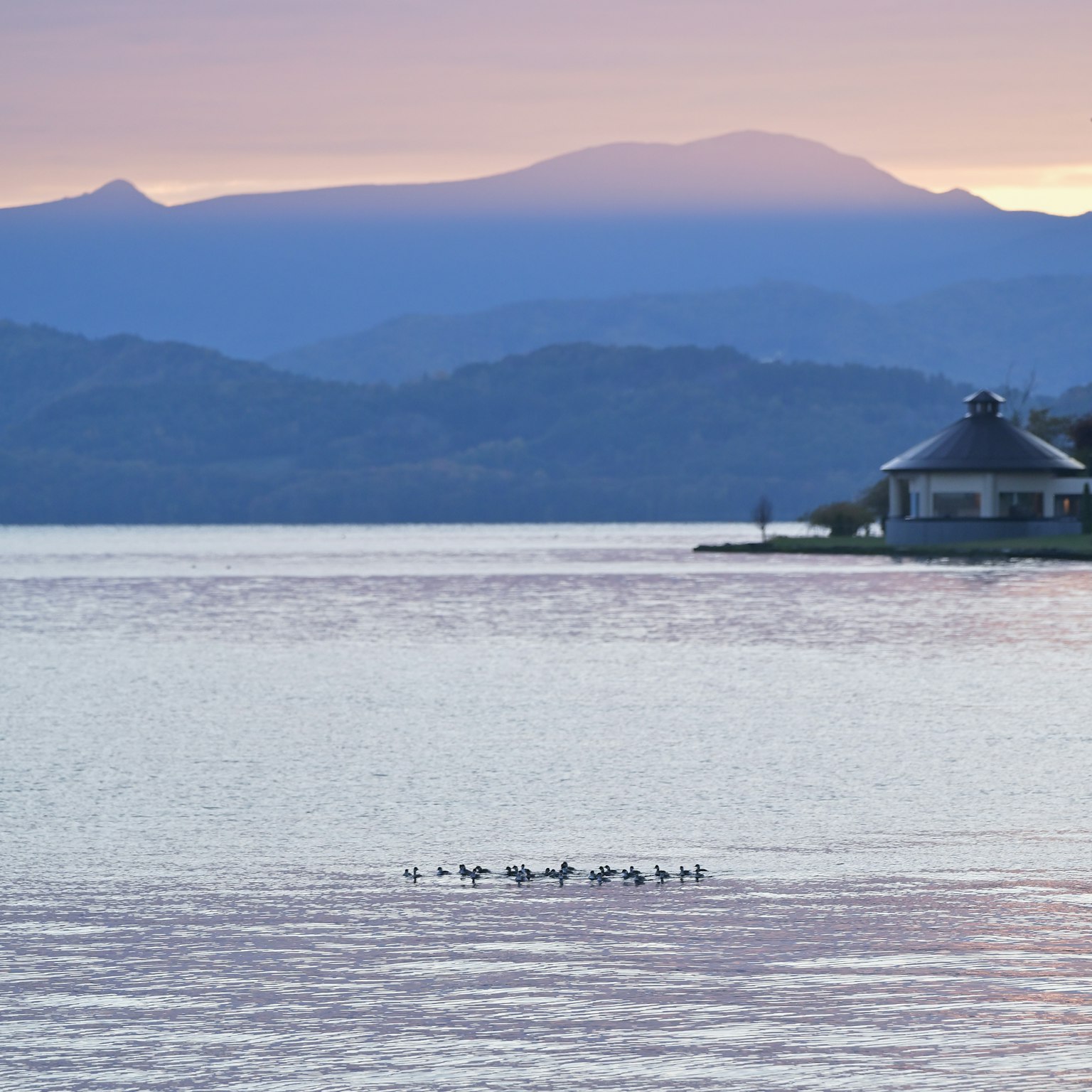 湖の静かな風景に浮かぶ小屋と山々のシルエット