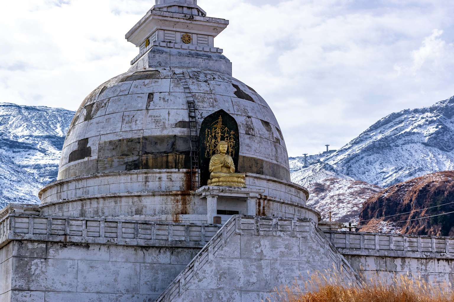 Stupa with a Buddha statue against a snow-covered mountain backdrop
