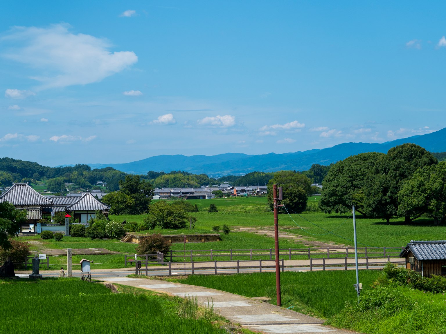 Rural landscape under blue sky featuring fields and distant mountains