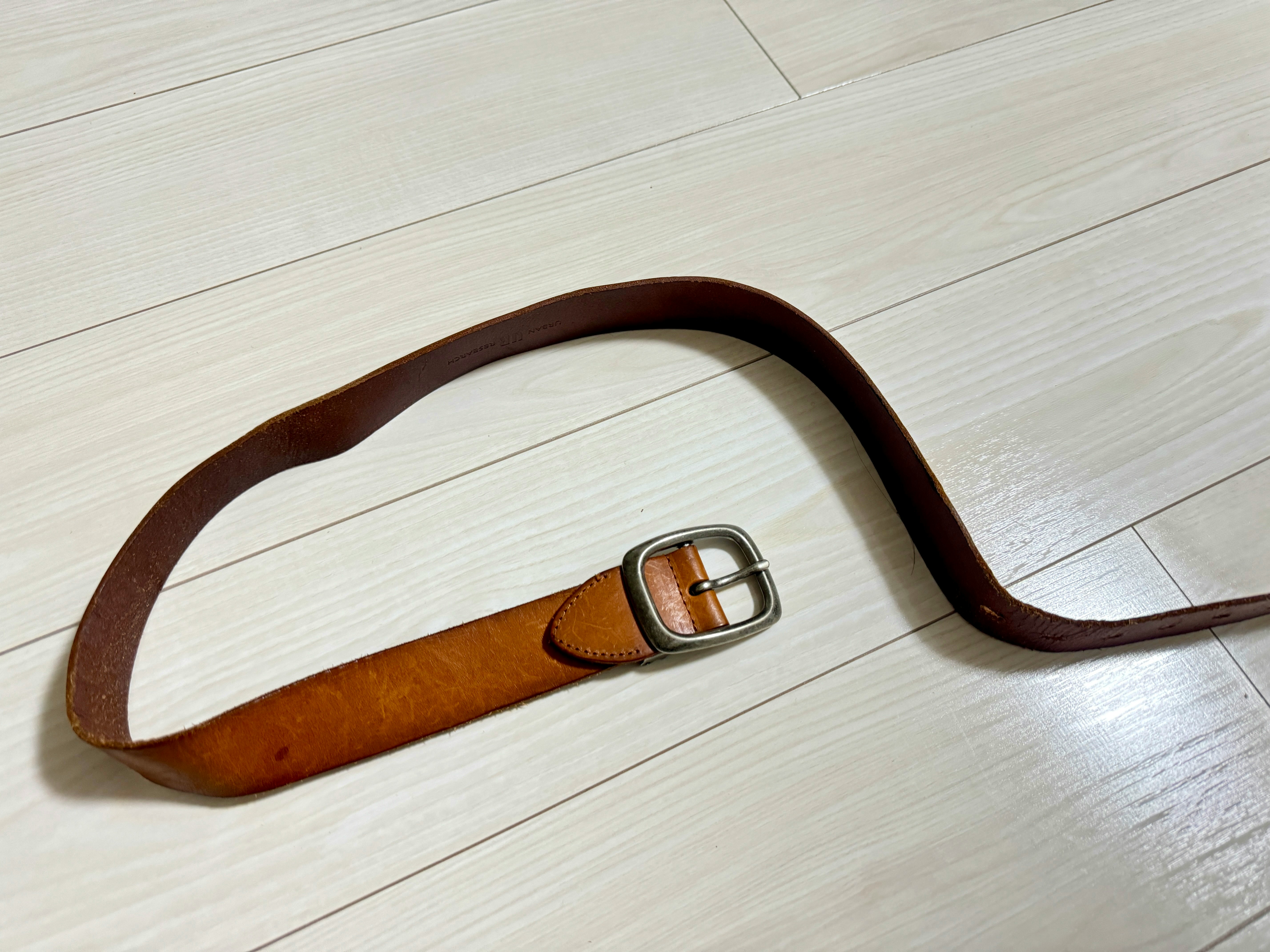 フローリングの上に置かれた革ベルトのバックル付き