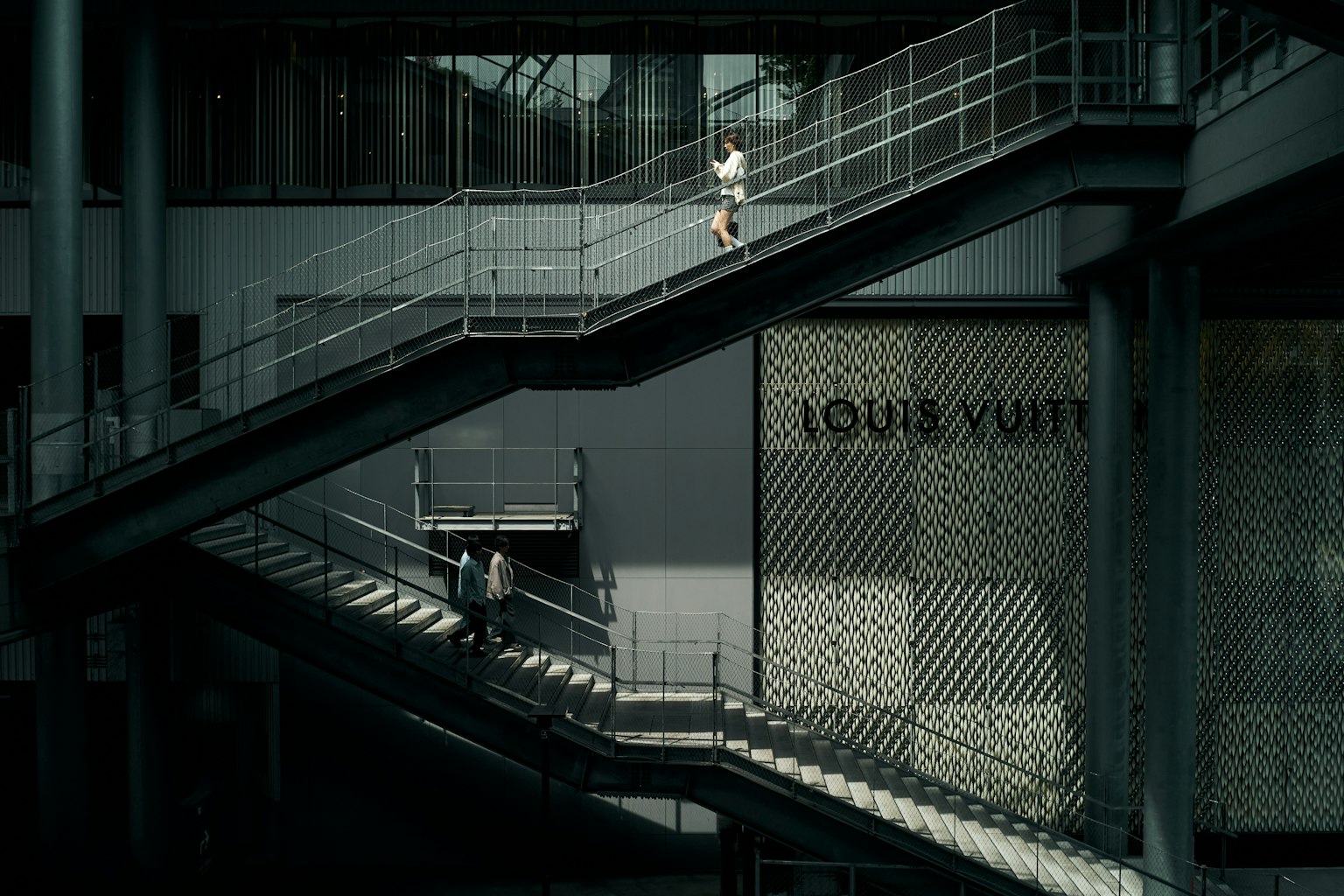 Scene of a person ascending and another descending stairs with a Louis Vuitton store in view