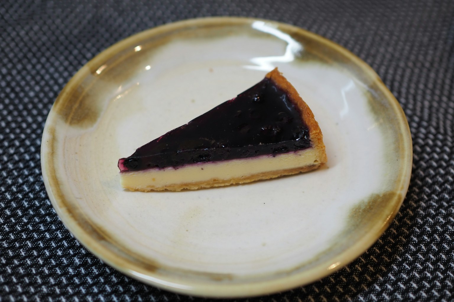Ein Stück Käsekuchen mit schwarzen Beeren auf einem dekorativen Teller