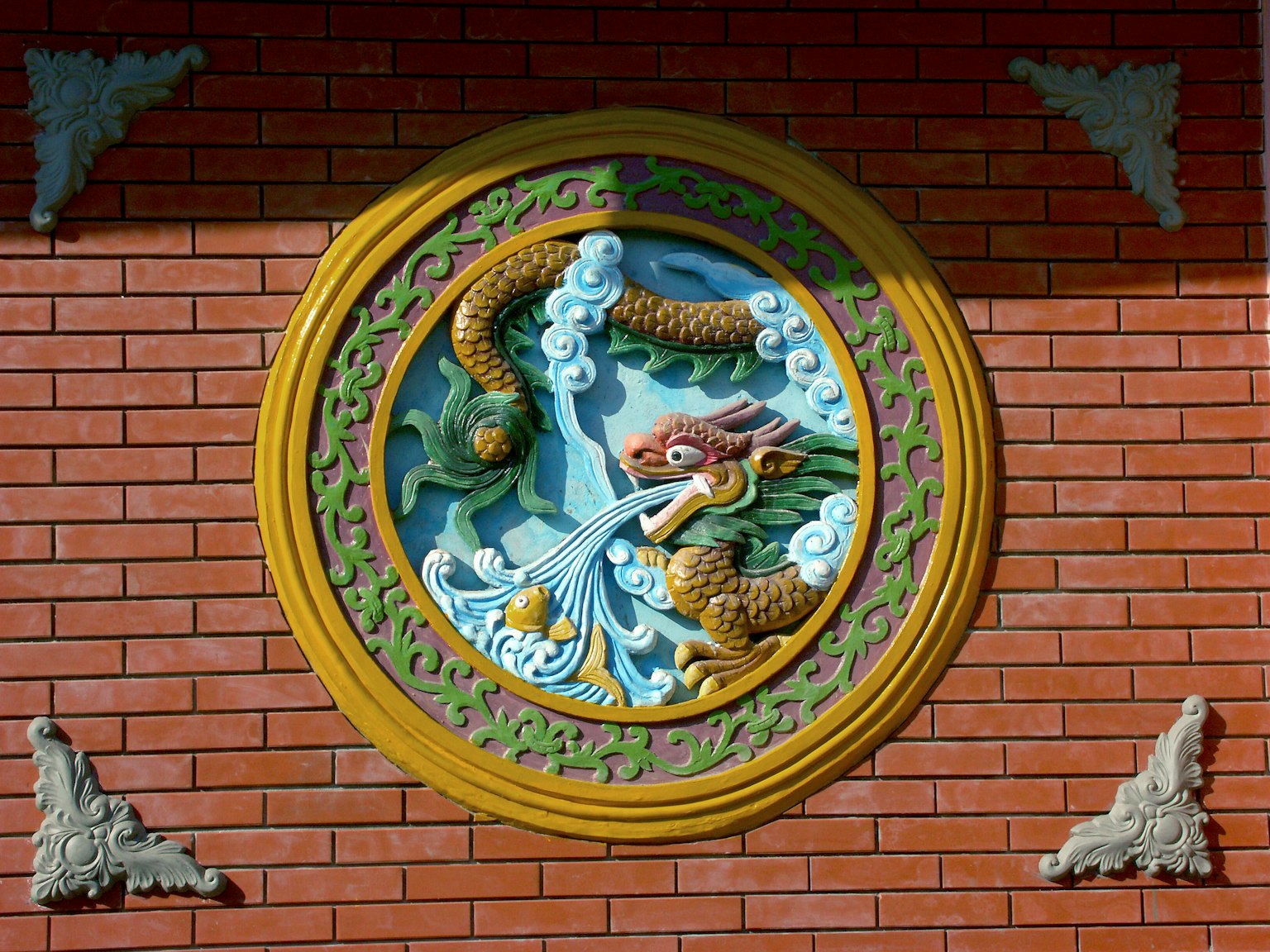 A decorative dragon sculpture spouting water on a red brick wall