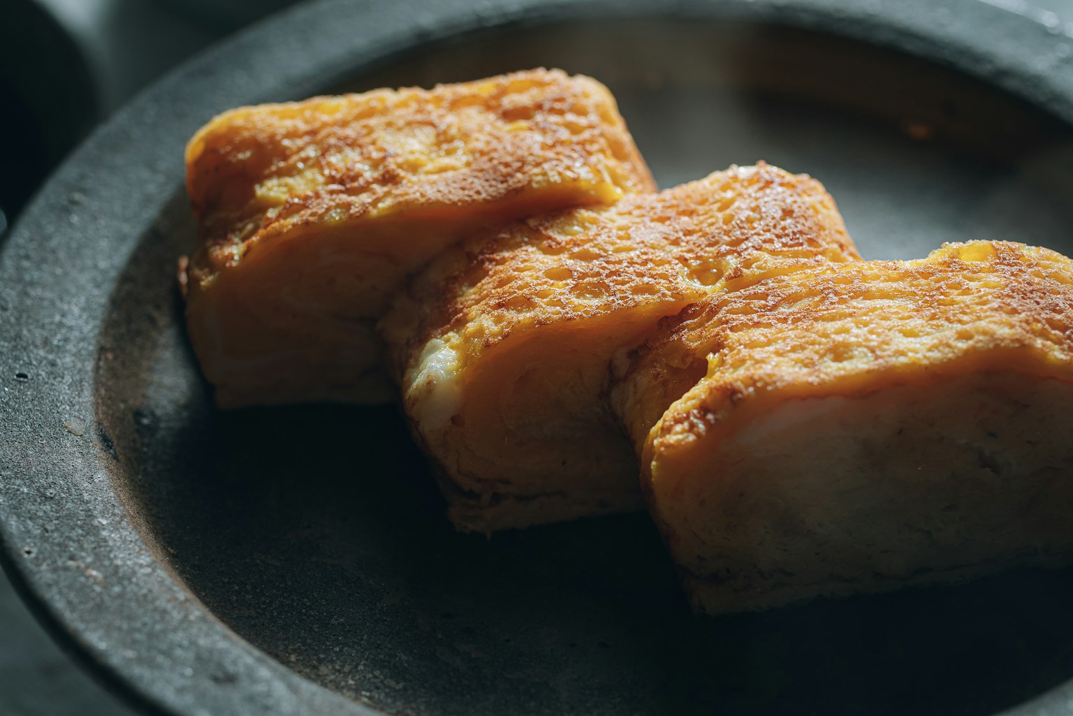 Trois morceaux de tofu doré sur une assiette sombre