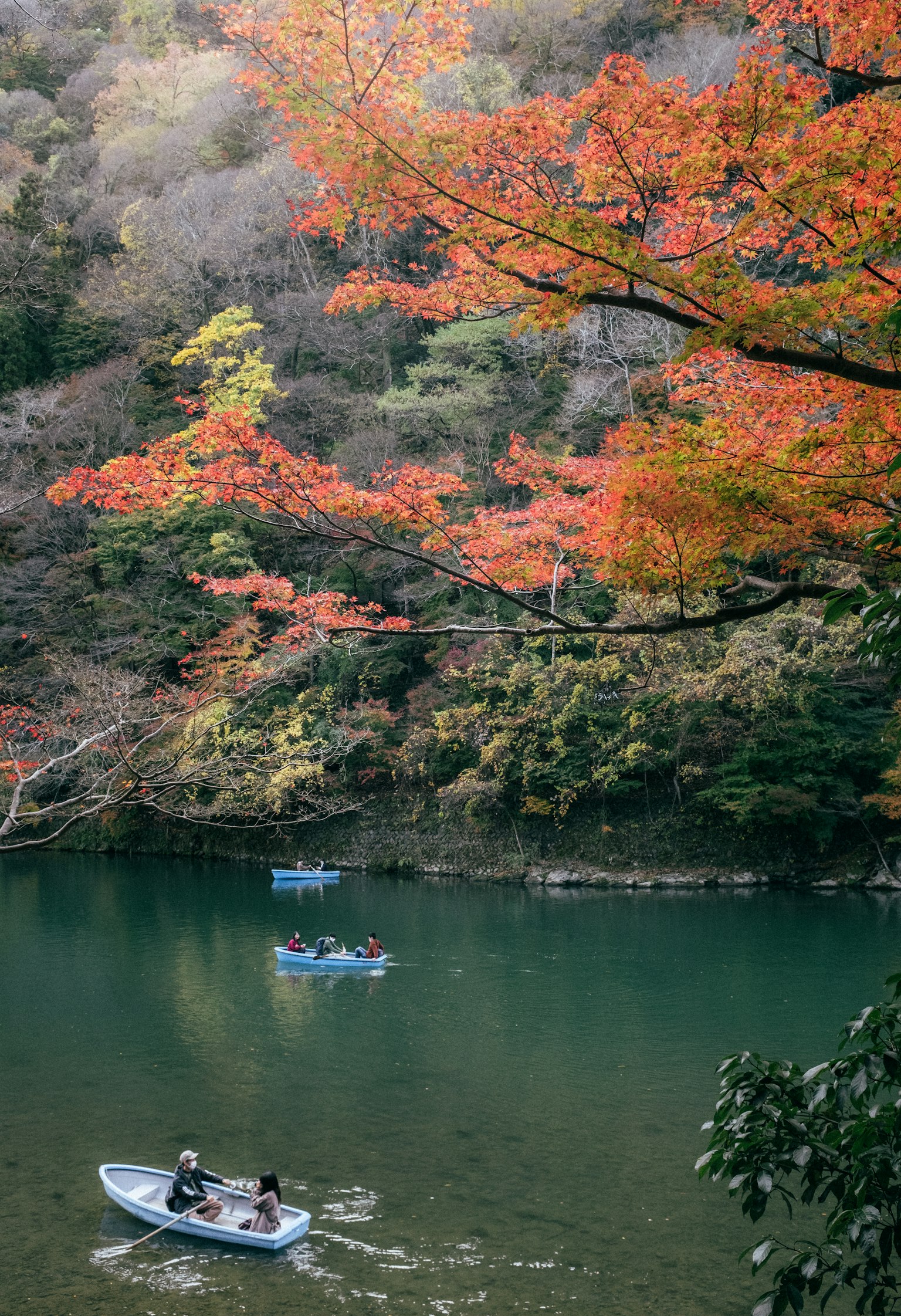 People in boats on a tranquil lake surrounded by vibrant autumn foliage