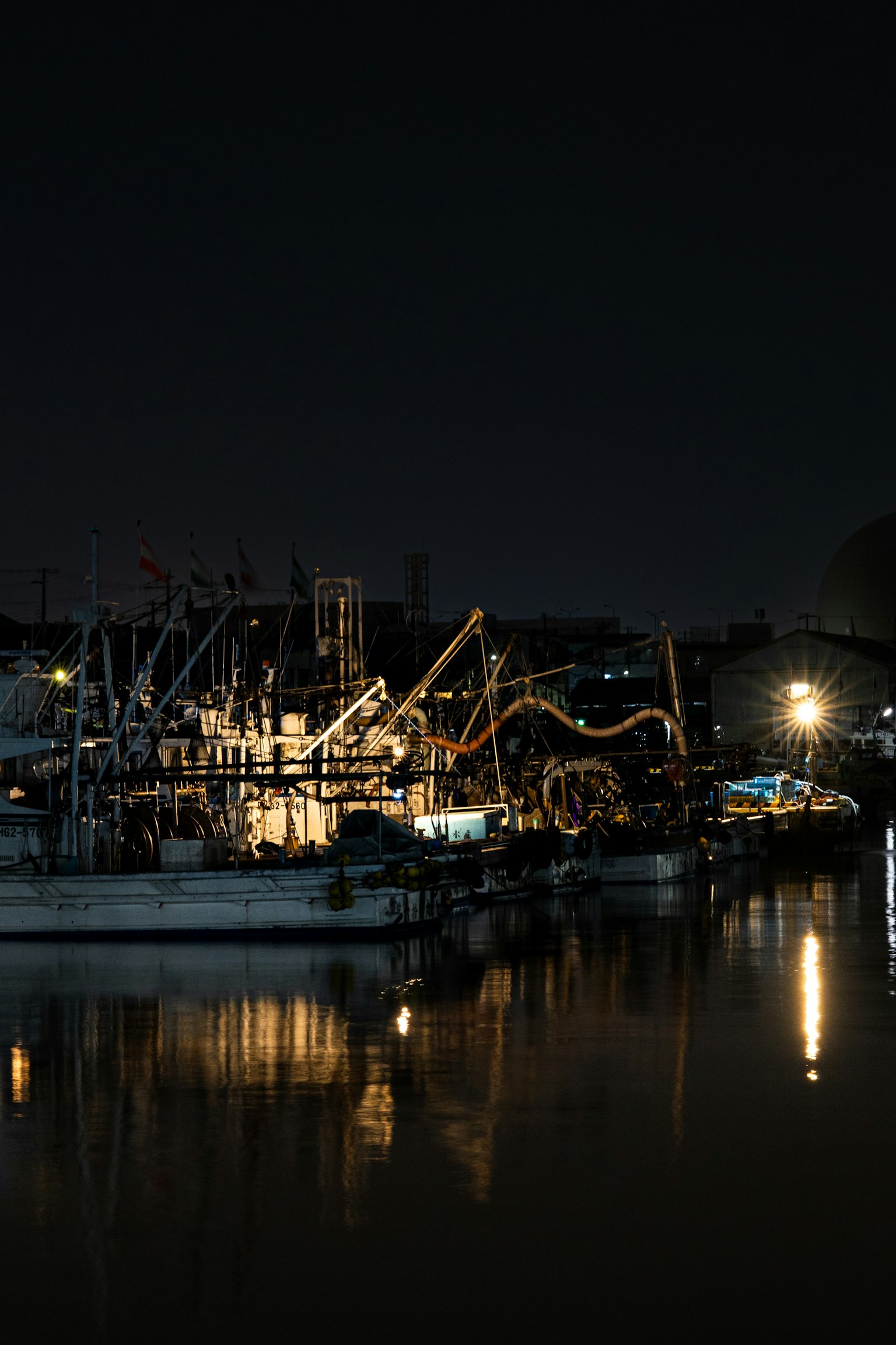 Barcos de pesca y luces del puerto reflejados en el agua por la noche