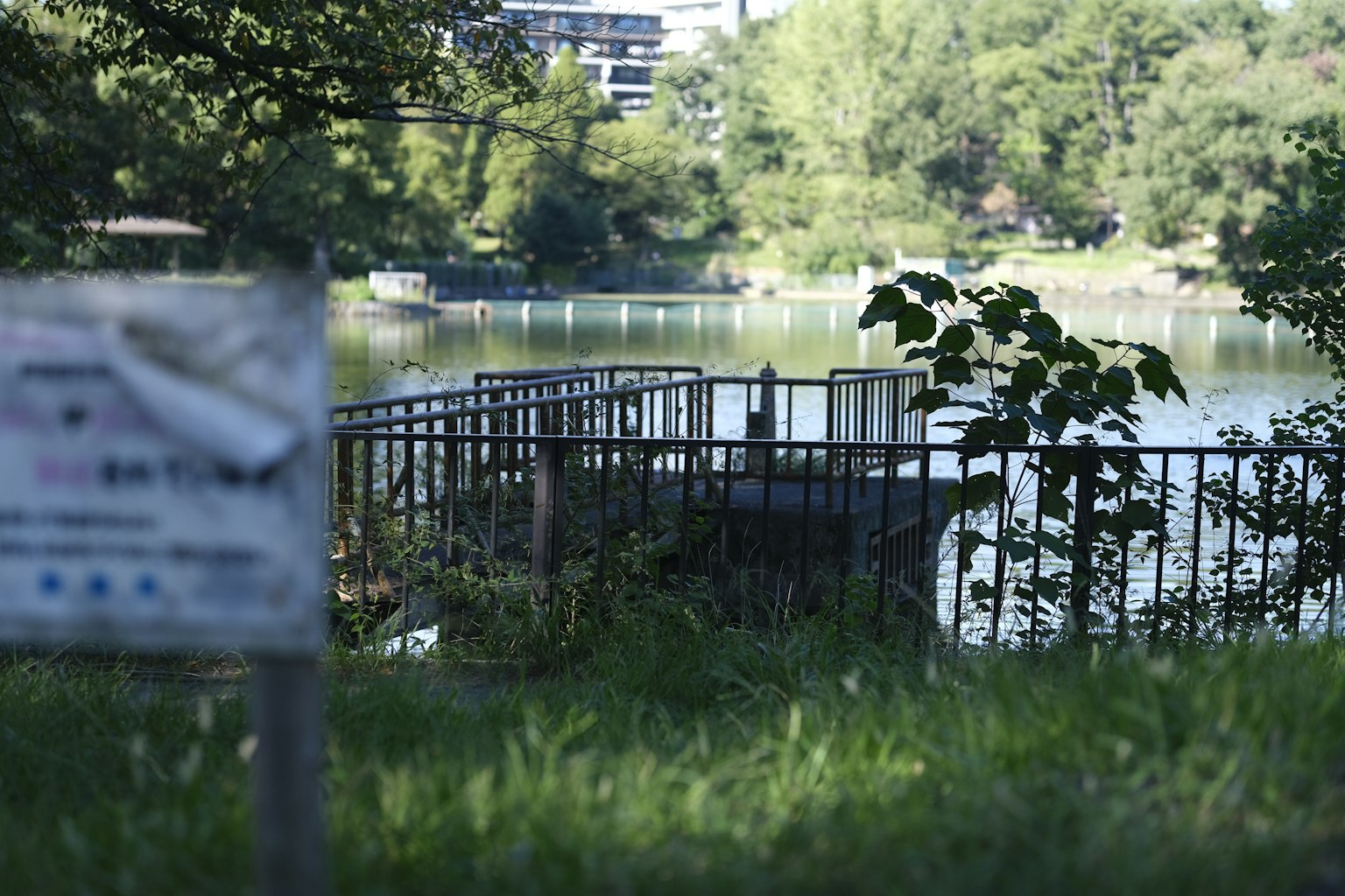 Valla y señal cerca de un lago rodeado de hierba verde y árboles