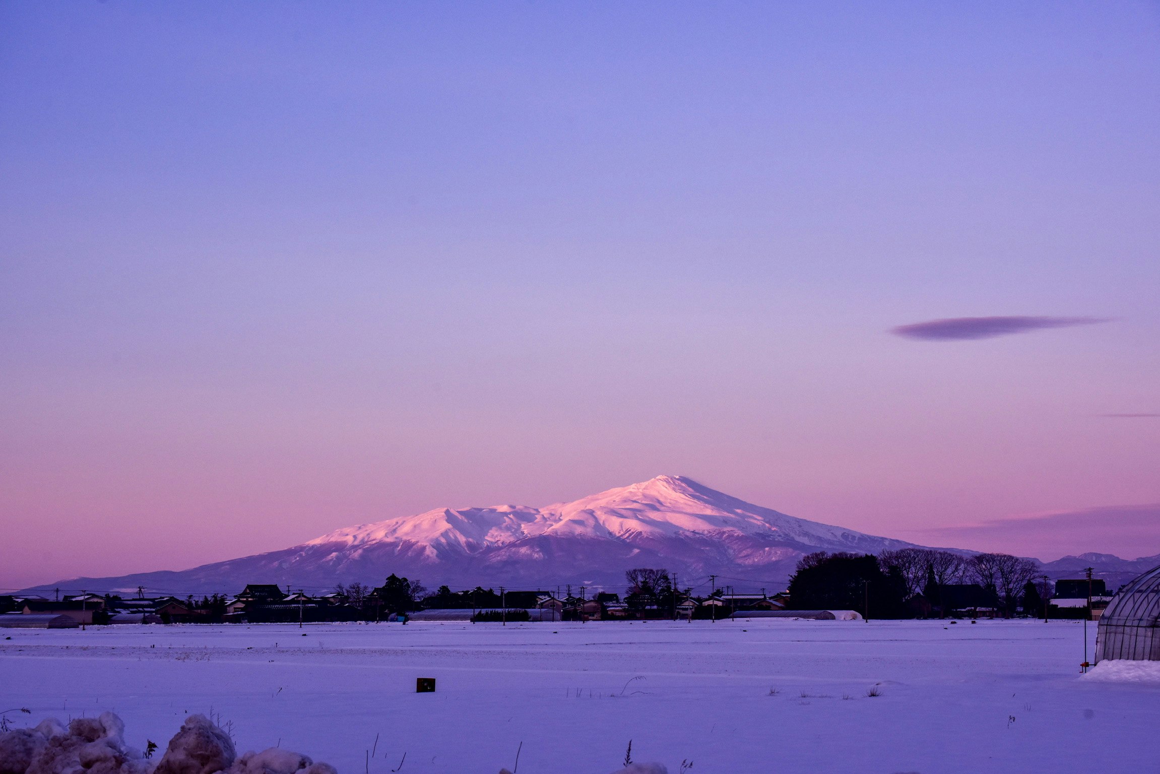 夕日に染まる鳥海山と雪原の冬景色