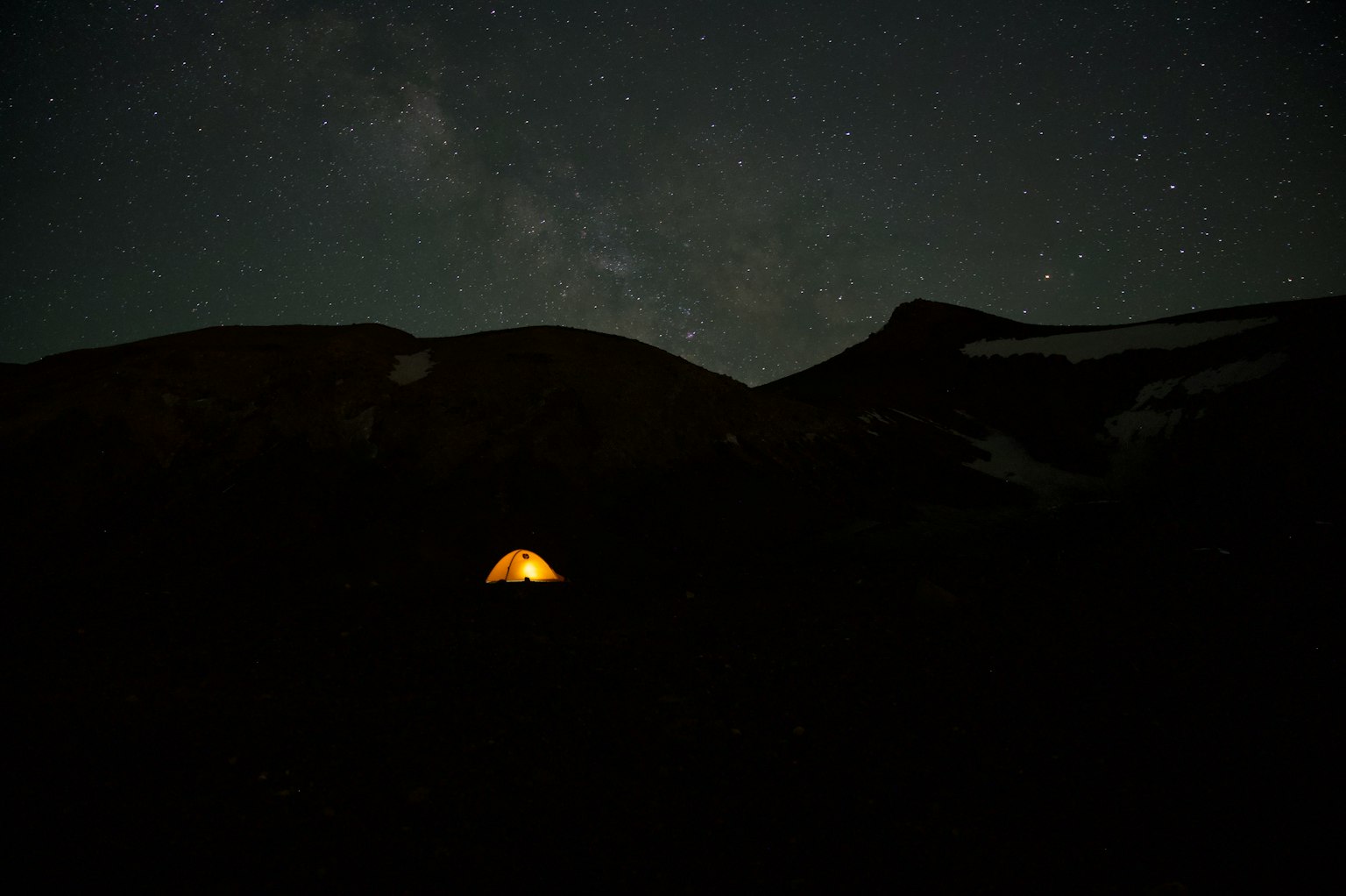 A bright tent illuminated under a starry night sky