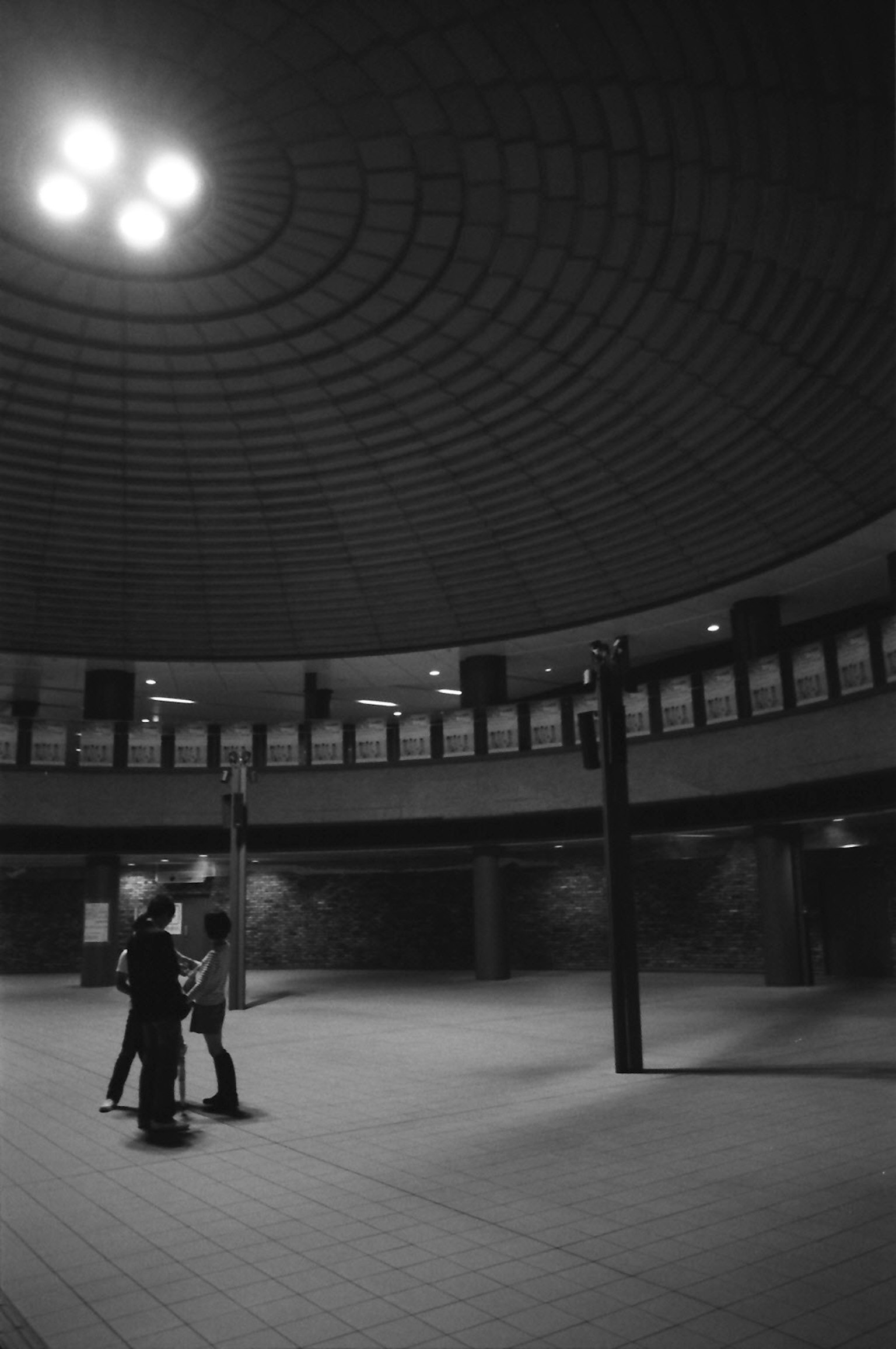 Two figures standing in a circular, monochrome space with a textured ceiling