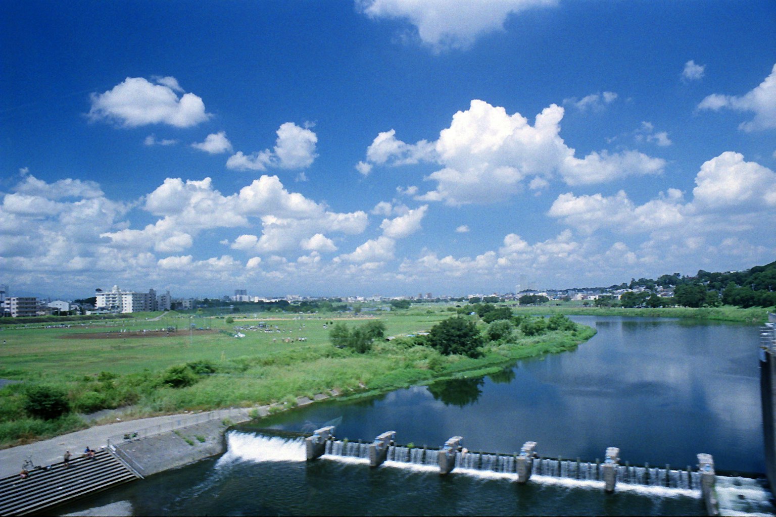 Malersicher Ausblick mit blauem Himmel und weißen Wolken grünen Feldern und fließendem Fluss