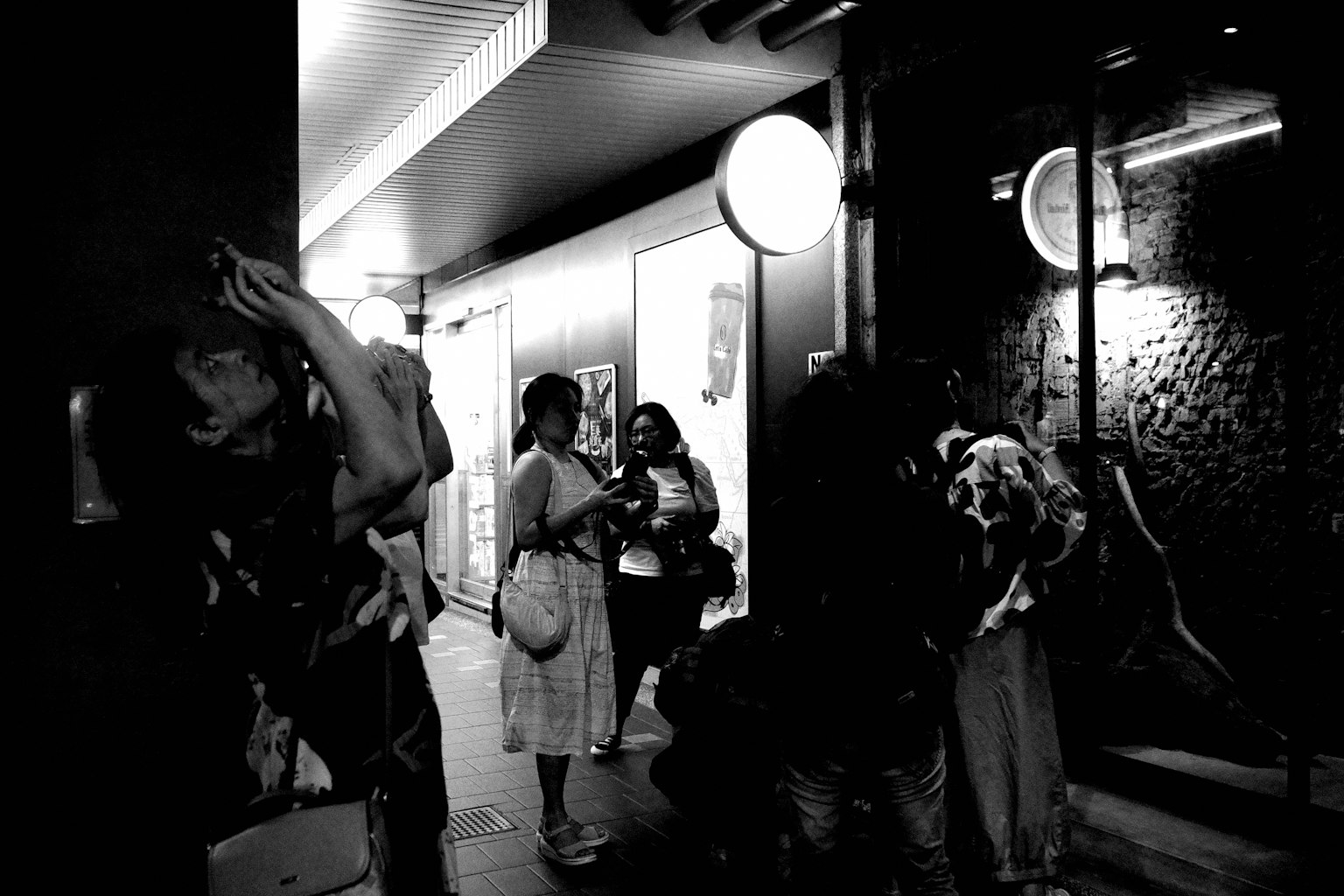 夜の街角で人々が集まるシーン 白黒の写真で、明るい照明と暗い背景が対比されている