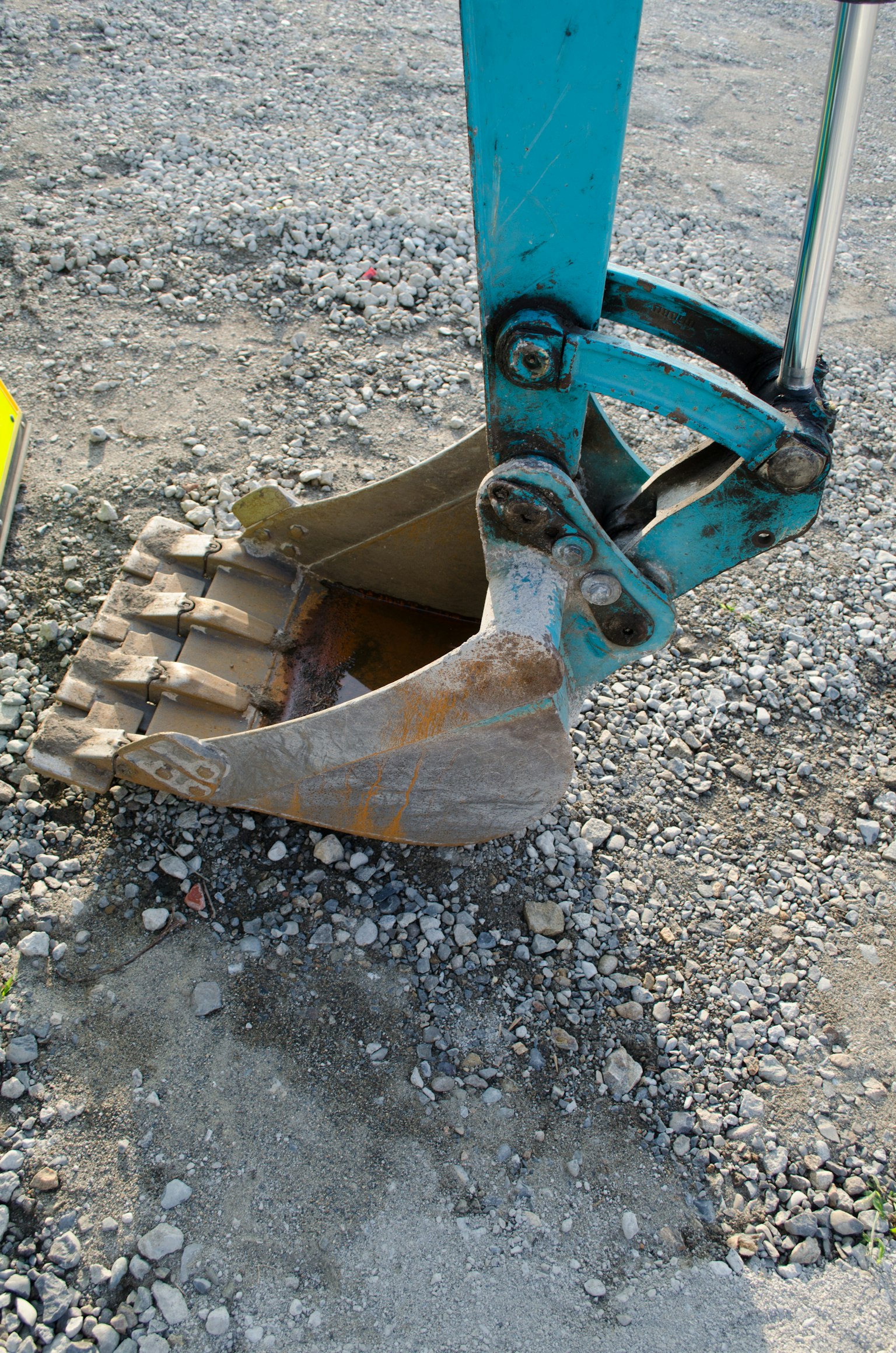 A close-up of a hydraulic excavator bucket resting on gravel