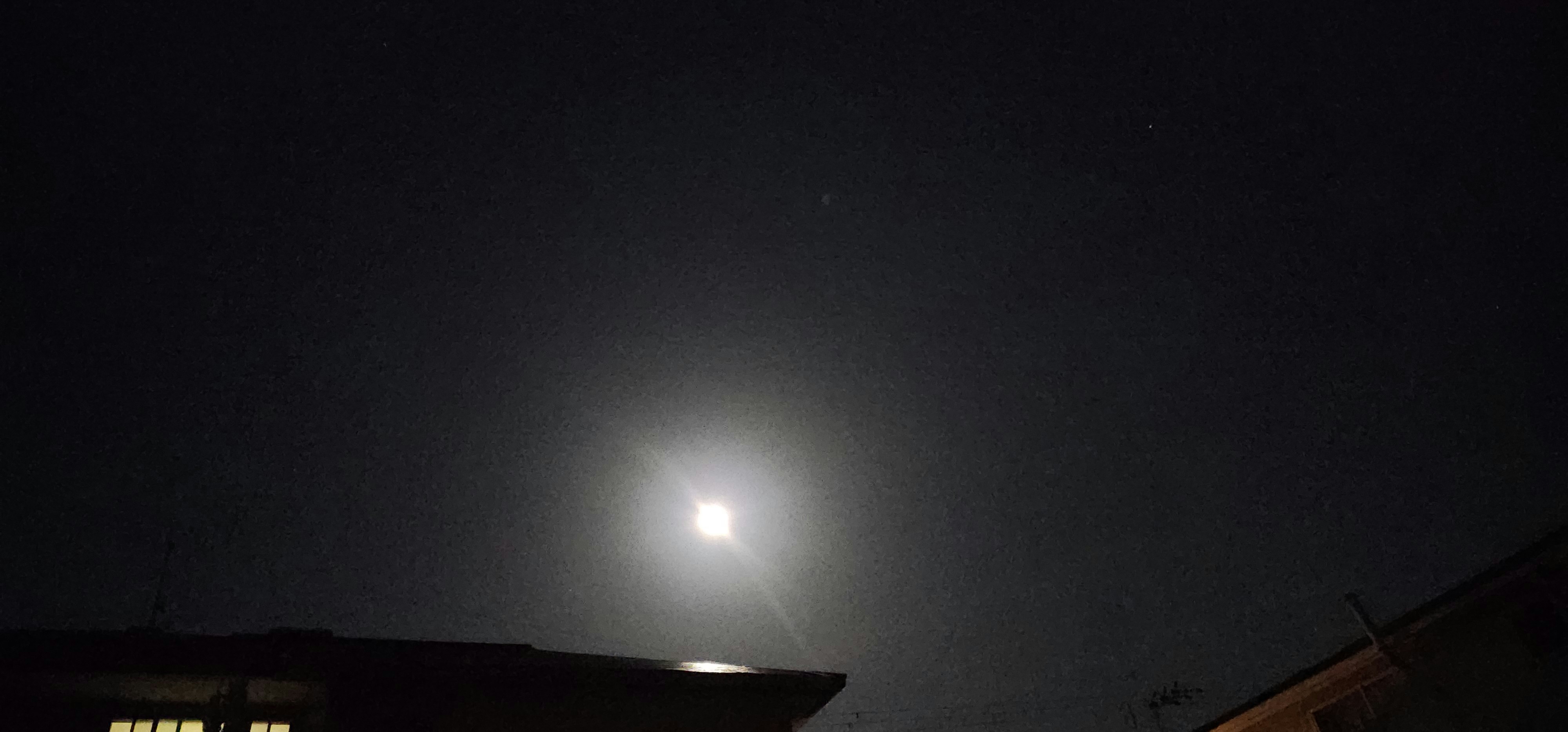 夜空に浮かぶ月光のような光と街の屋根
