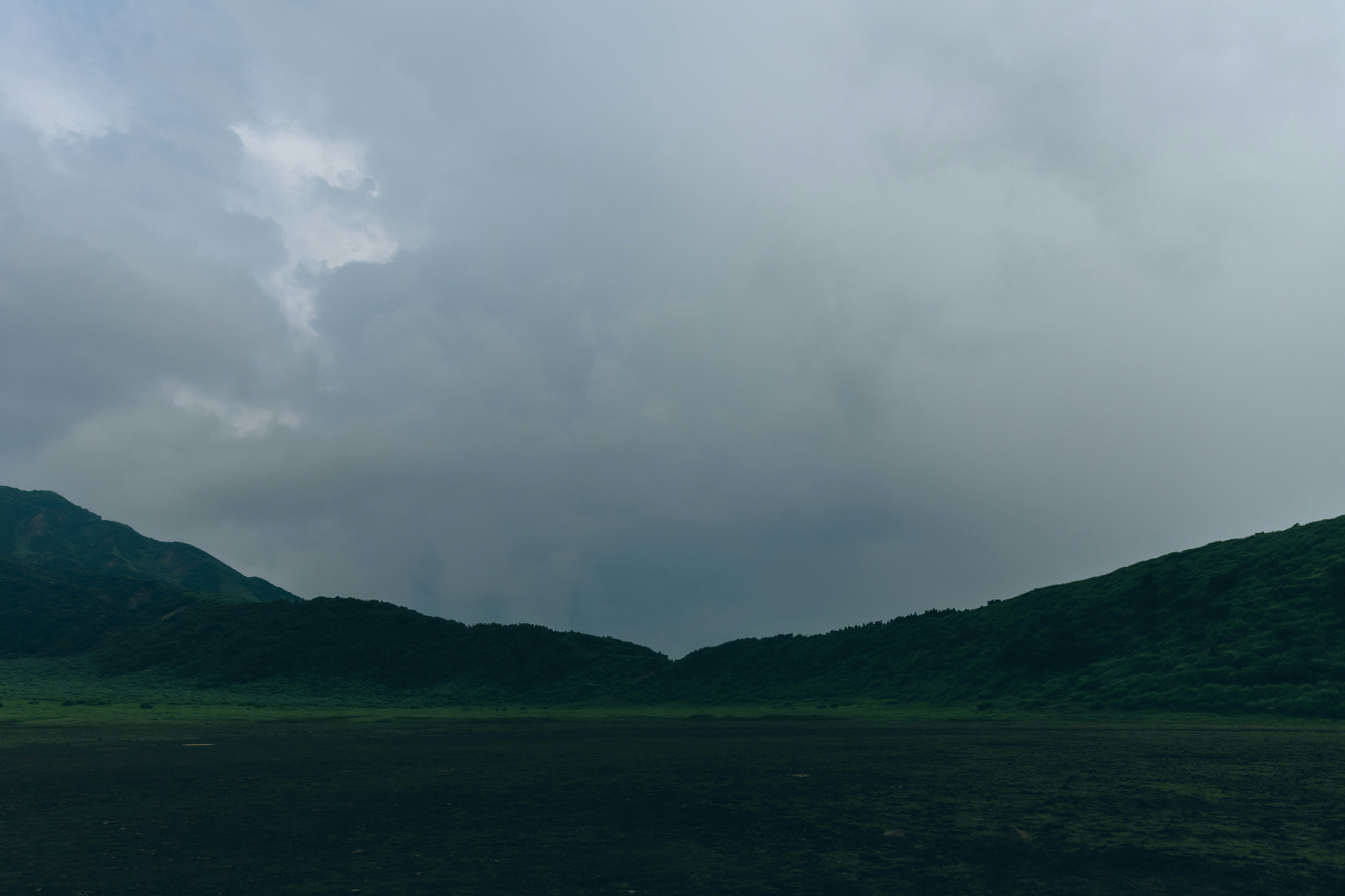 緑の谷と山並みを覆う曇り空の風景