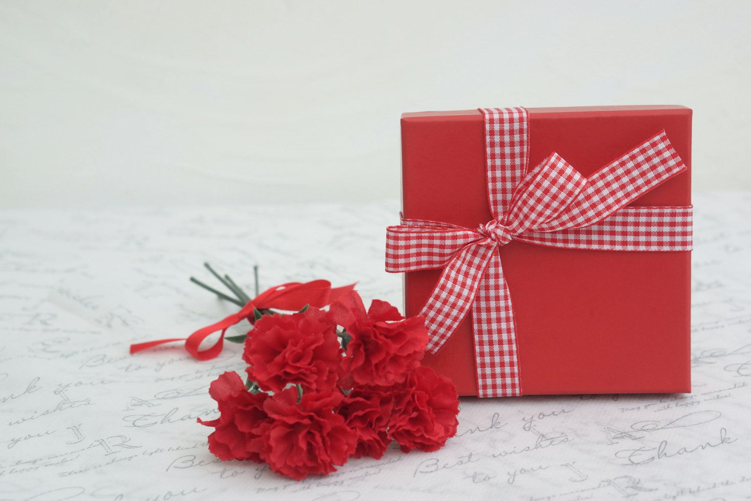 Scatola regalo rossa con nastro a scacchi e bouquet di garofani rossi