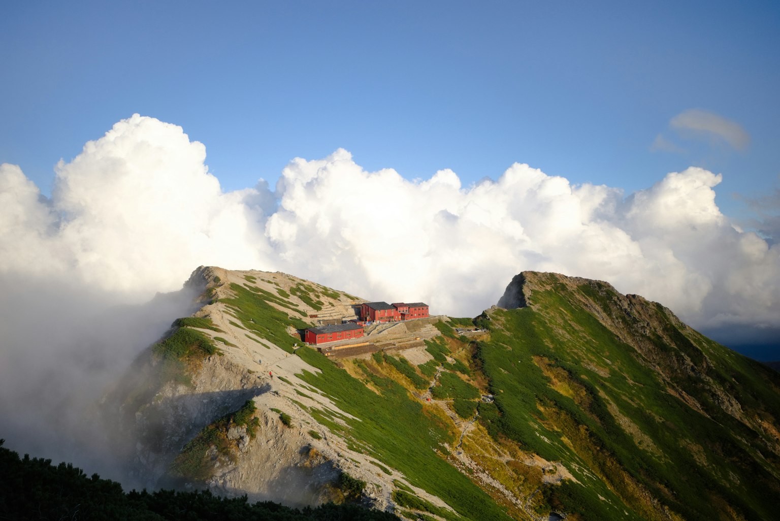 Red building on mountain peak surrounded by clouds
