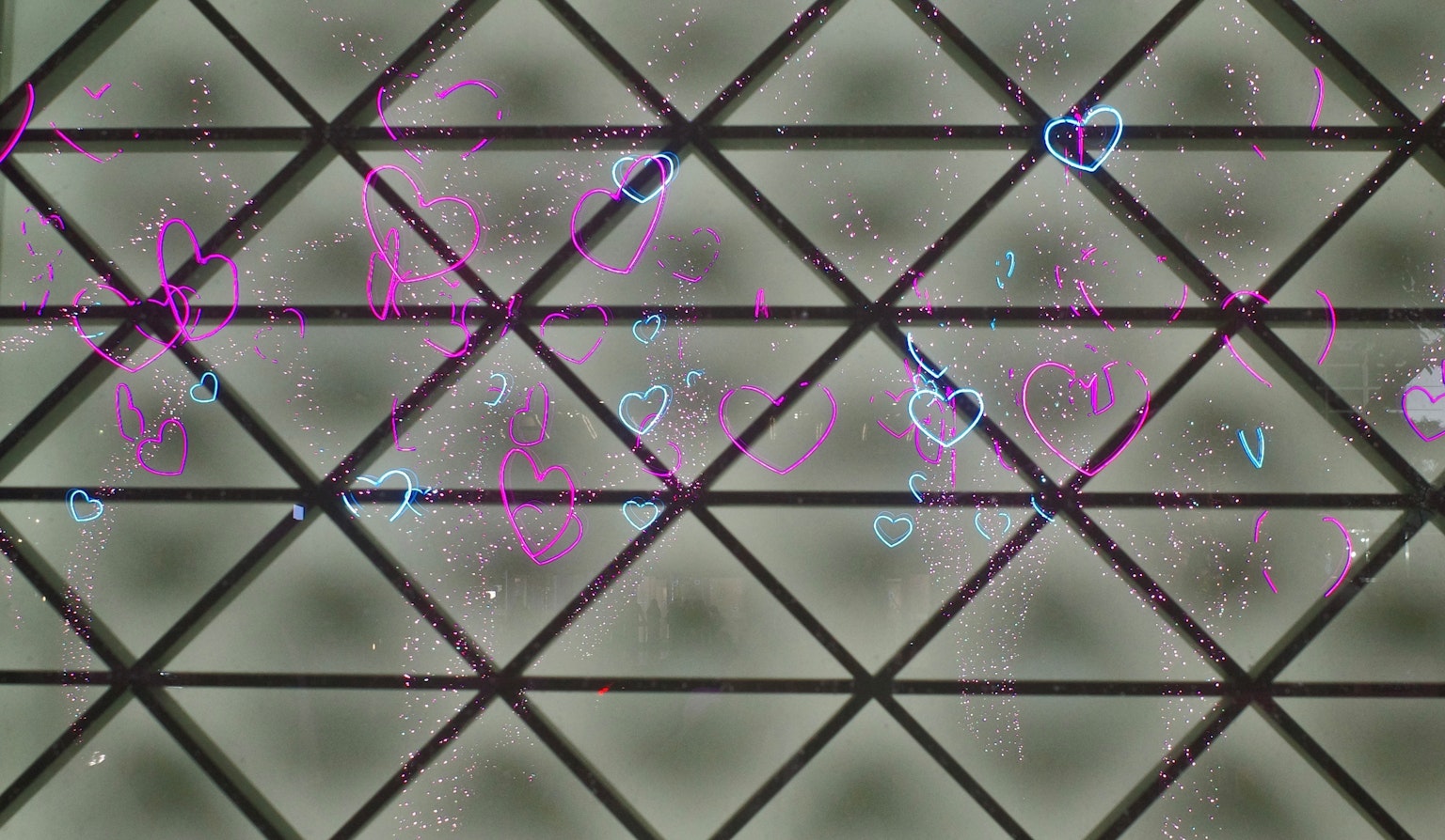 黒い格子模様の背景にピンクと青のハートのグラフィティが描かれている