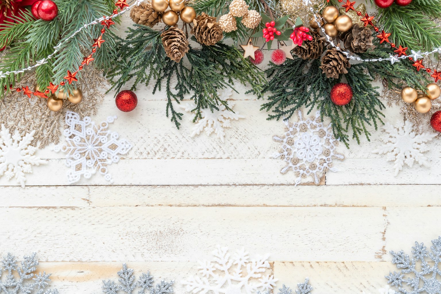 Decorazione natalizia con foglie di pino ornamenti rossi accenti dorati e fiocchi di neve su uno sfondo di legno bianco