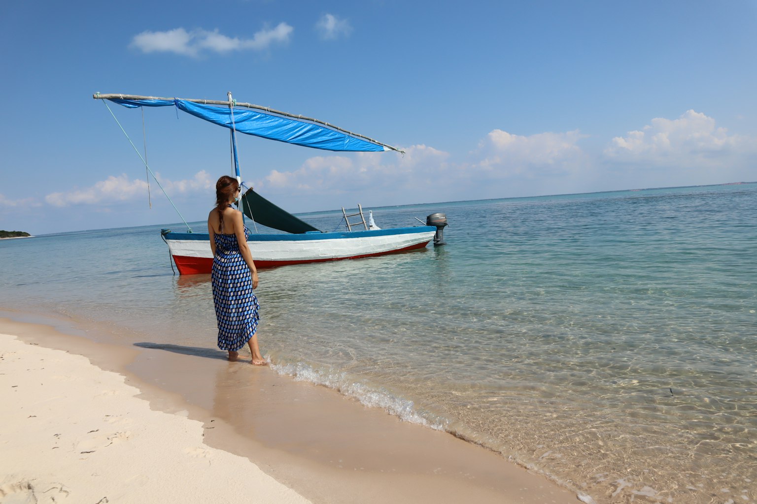 ผู้หญิงถือร่มสีน้ำเงินยืนอยู่บนชายหาดที่สวยงามมองไปที่ทะเลที่สงบ