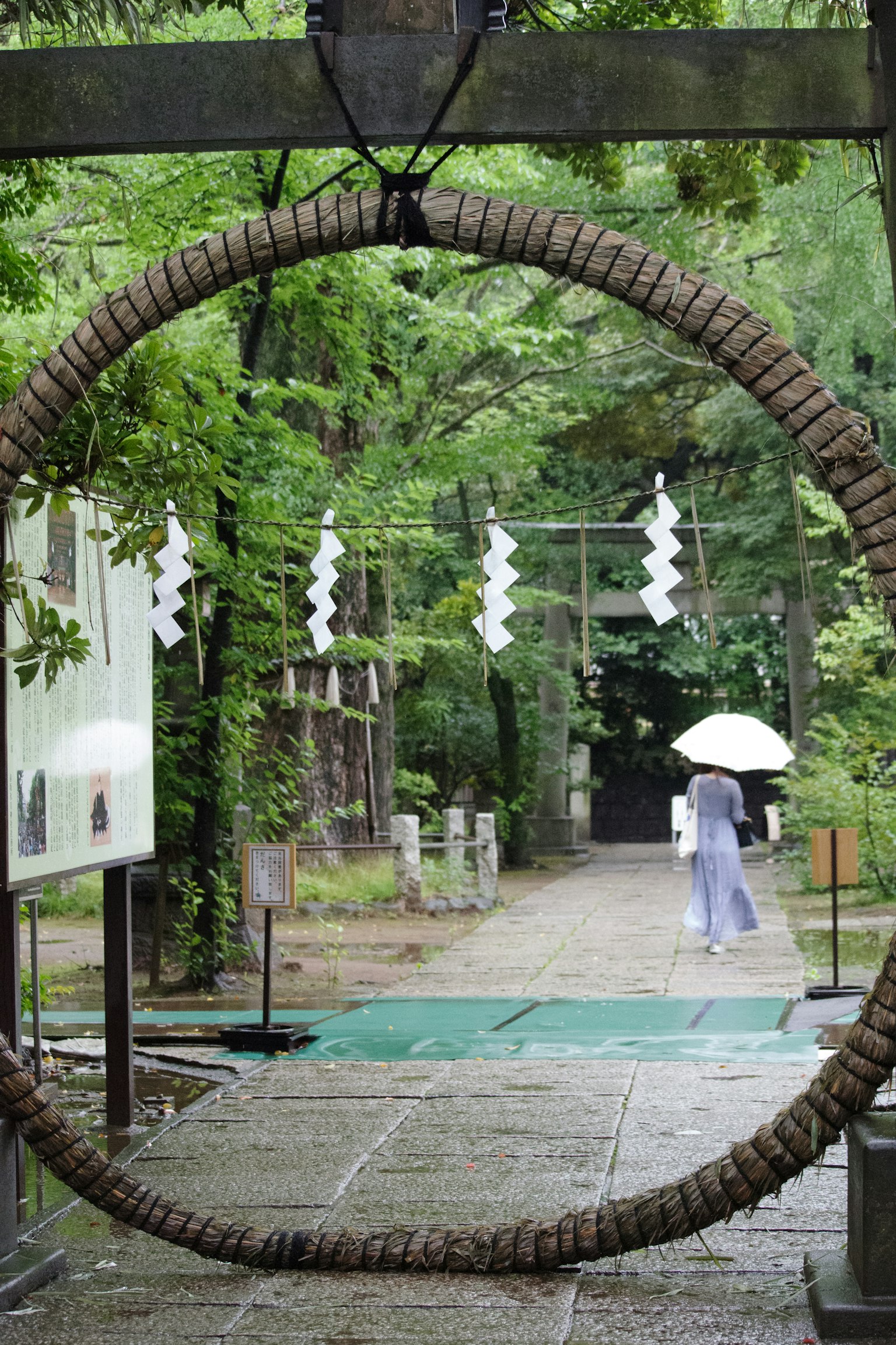 A large straw ring with white shimenawa decorations at a shrine entrance surrounded by lush greenery
