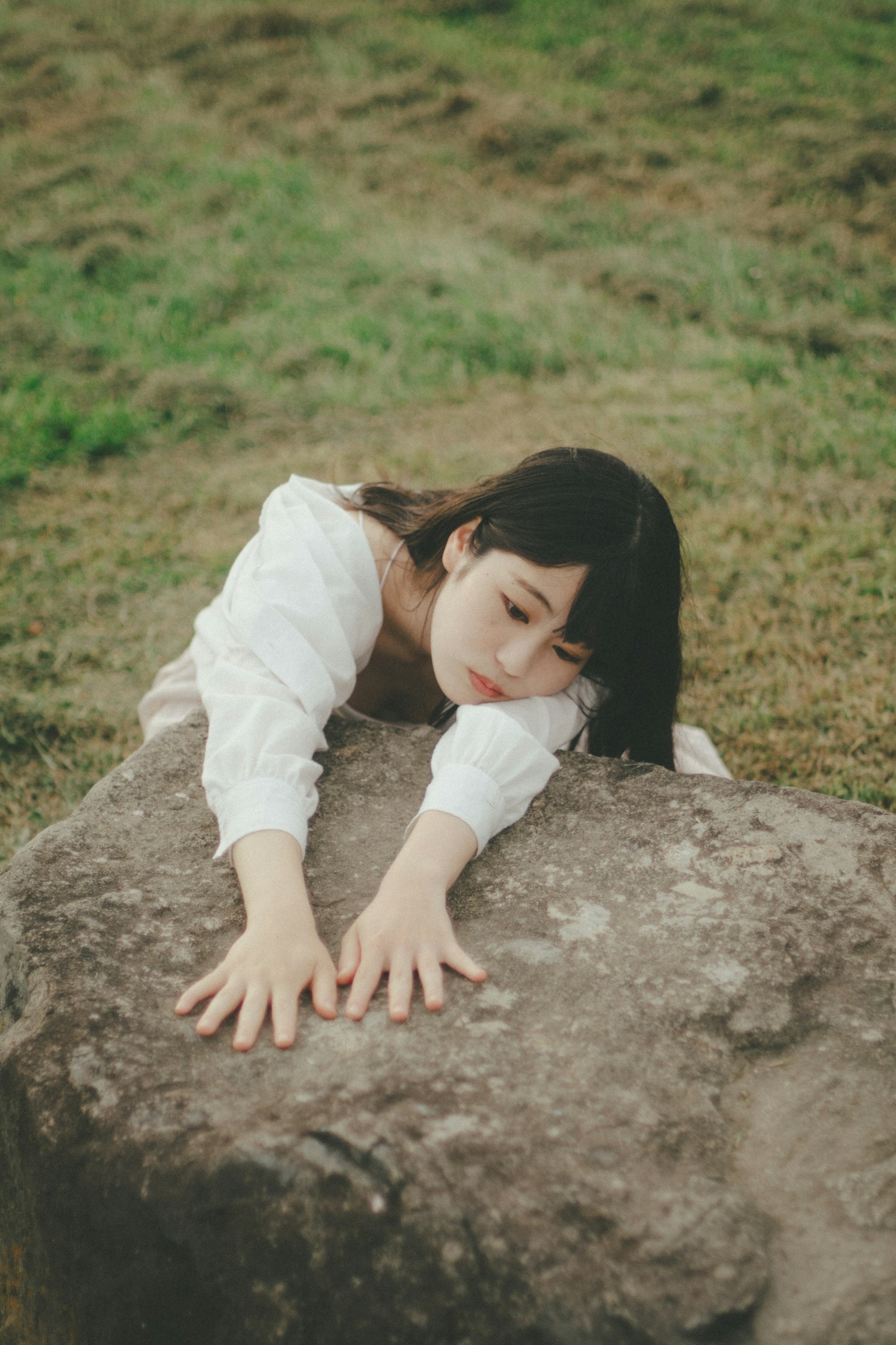 A woman posing on a stone in a grassy field