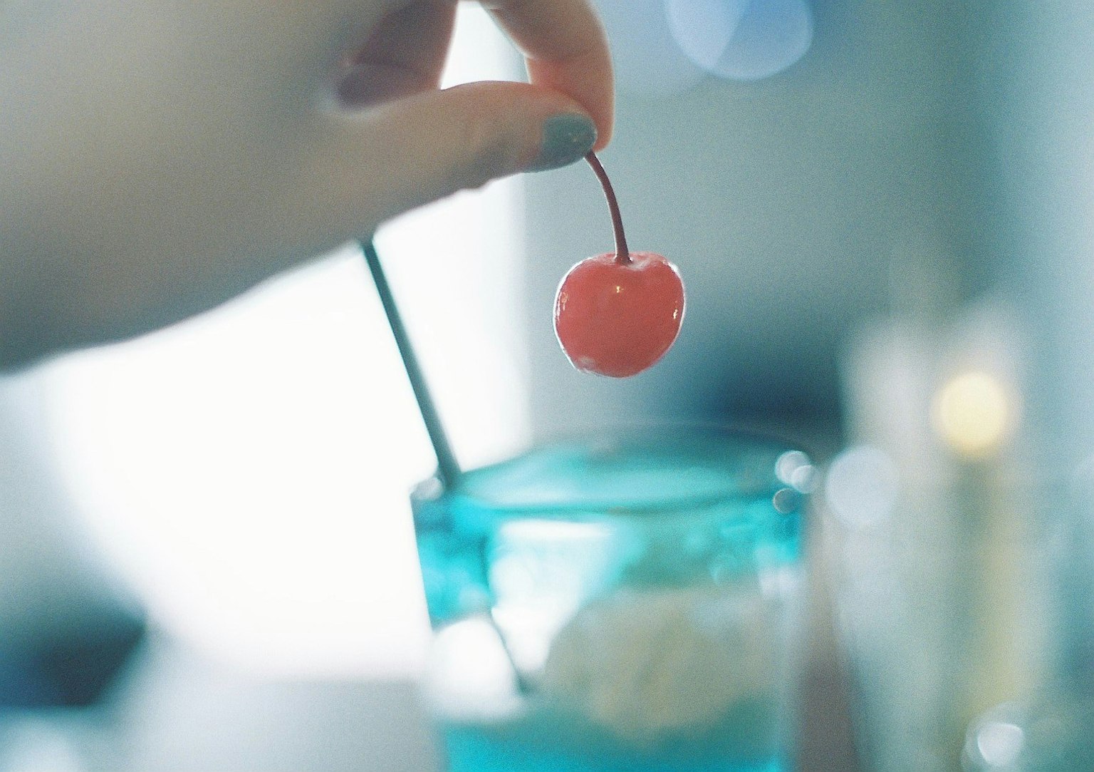 Una mano sosteniendo una cereza roja sobre una bebida azul