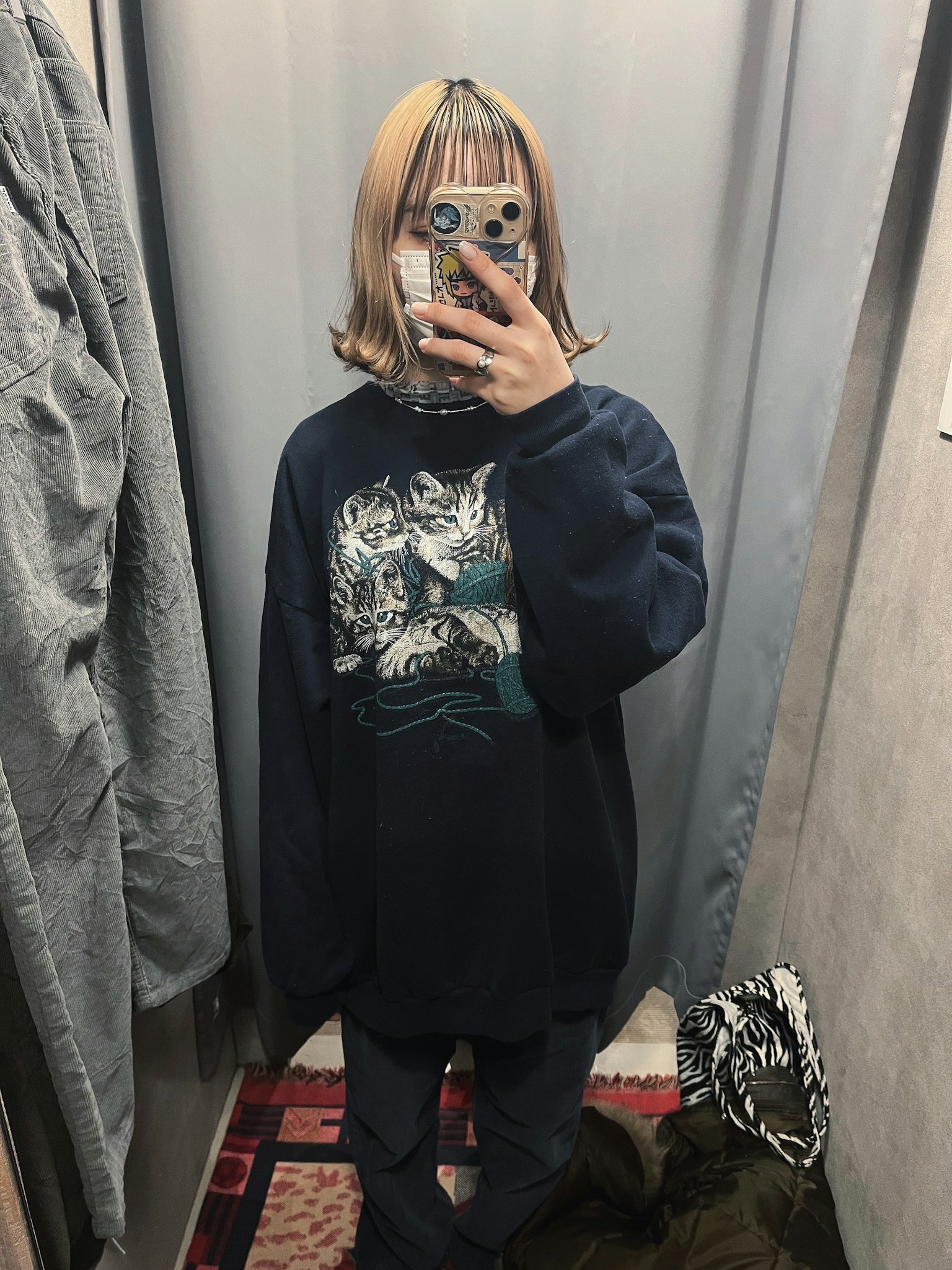 Femme jeune prenant un selfie dans un sweat bleu avec un motif de chat devant un rideau gris