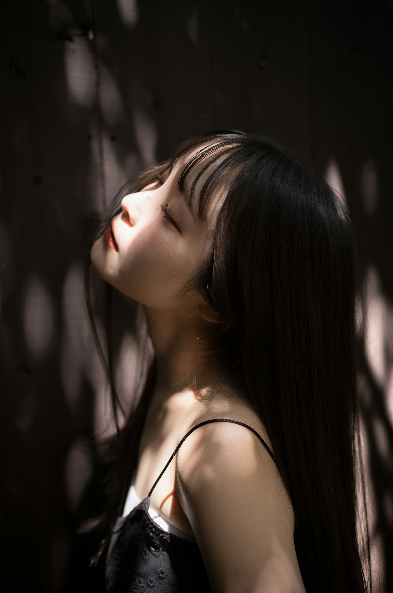 Una donna con capelli lunghi che guarda in alto nella luce soffusa e nelle ombre che evidenziano i suoi tratti