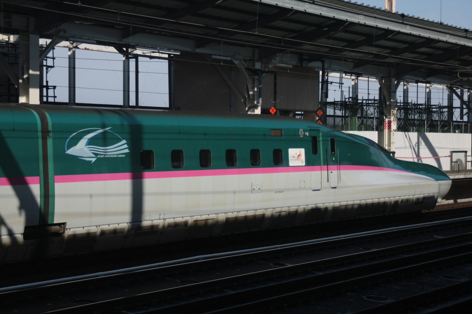 Seitenansicht eines Shinkansen an einem Bahnhof mit grünen und rosa Farben