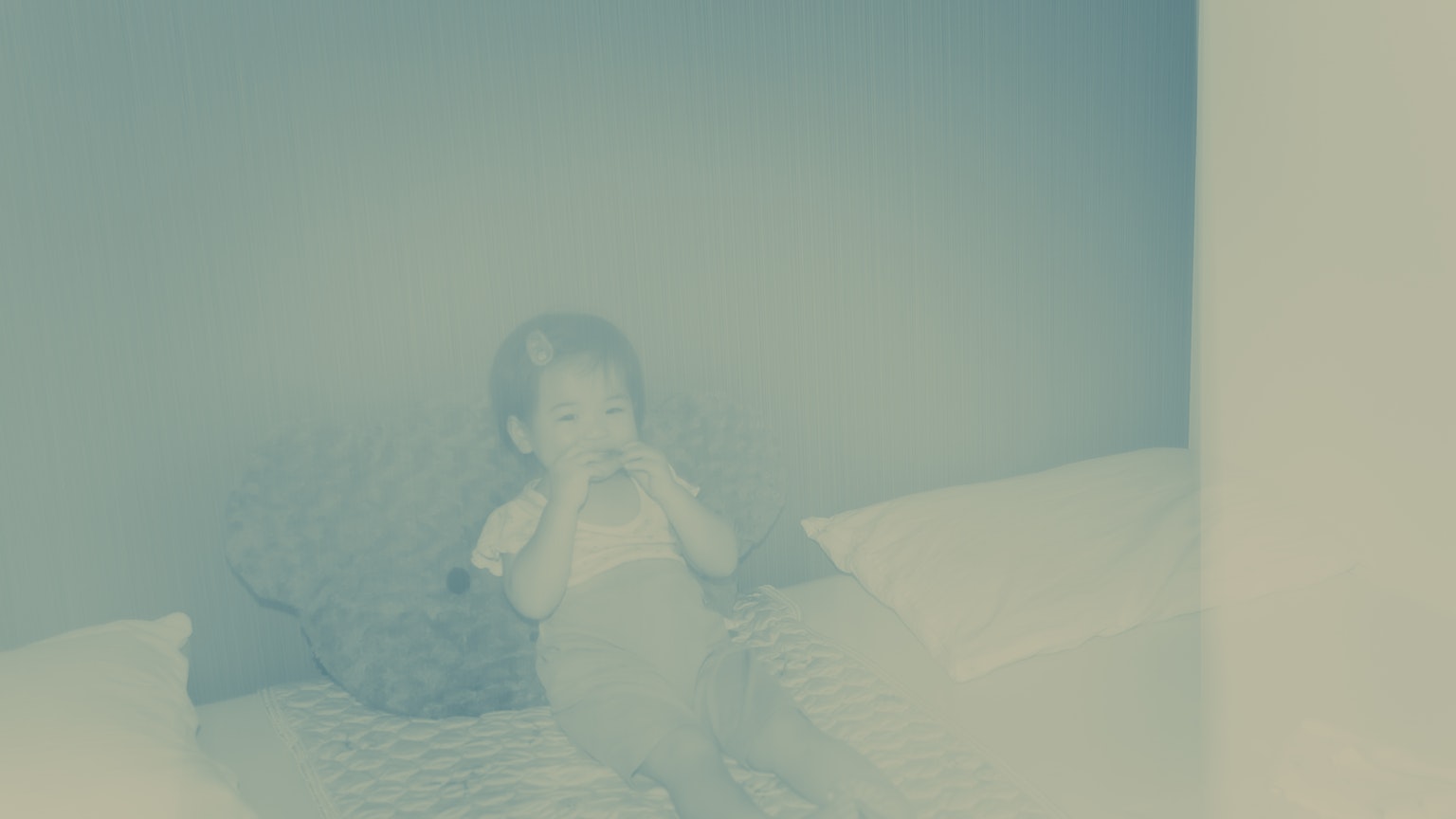 Một đứa trẻ ngồi trên giường với nền màu xanh