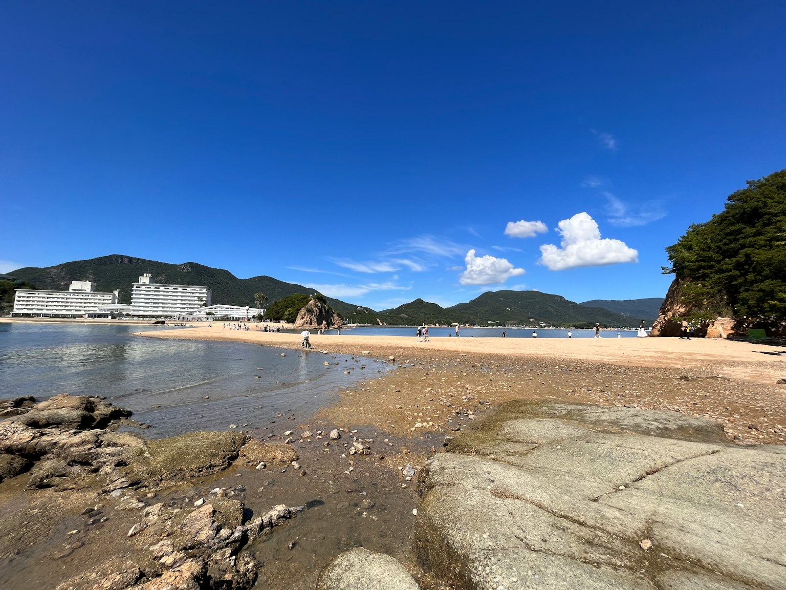 Küstenlandschaft unter blauem Himmel mit weißen Wolken, die Felsen und Sandstrand zeigt