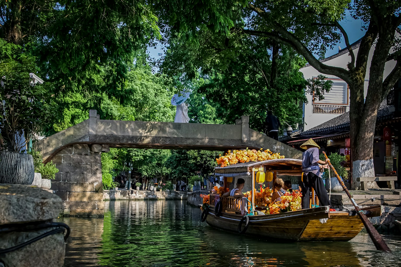 คลองที่สวยงามพร้อมเรือขนของใต้สะพานหินที่มีต้นไม้เขียวขจีล้อมรอบ
