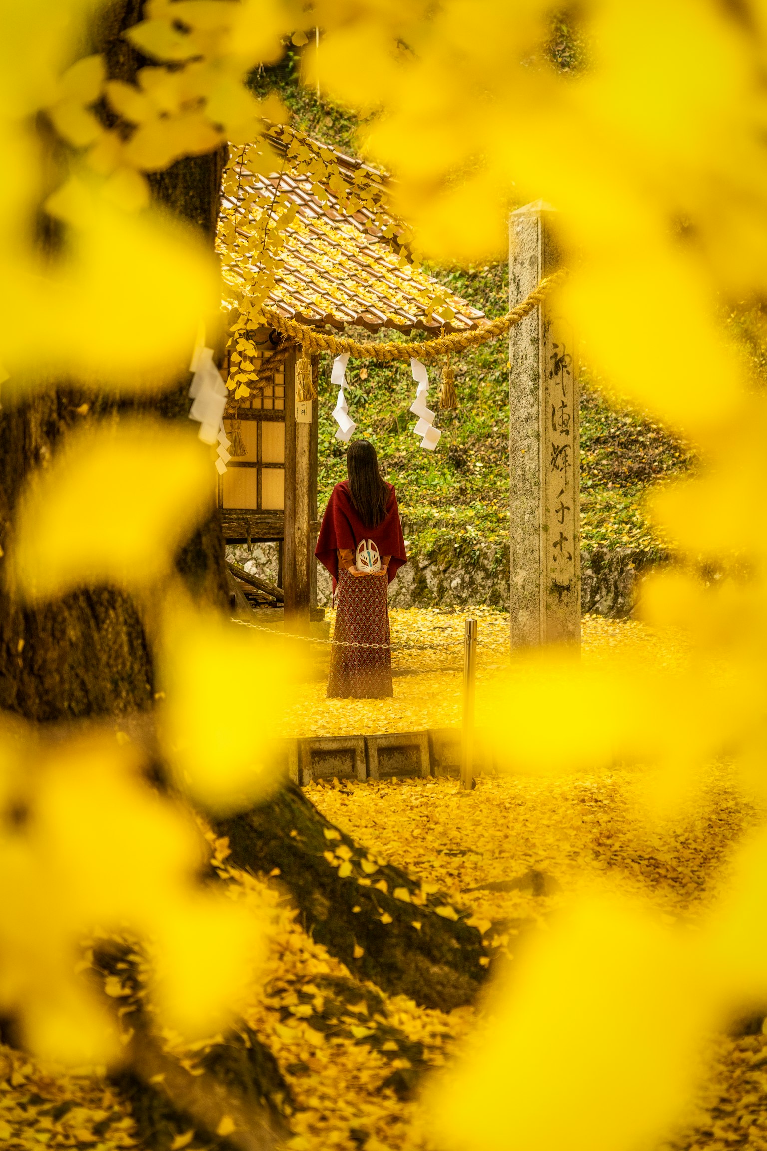 Mujer en kimono de pie frente a un edificio tradicional rodeada de hojas amarillas de ginkgo