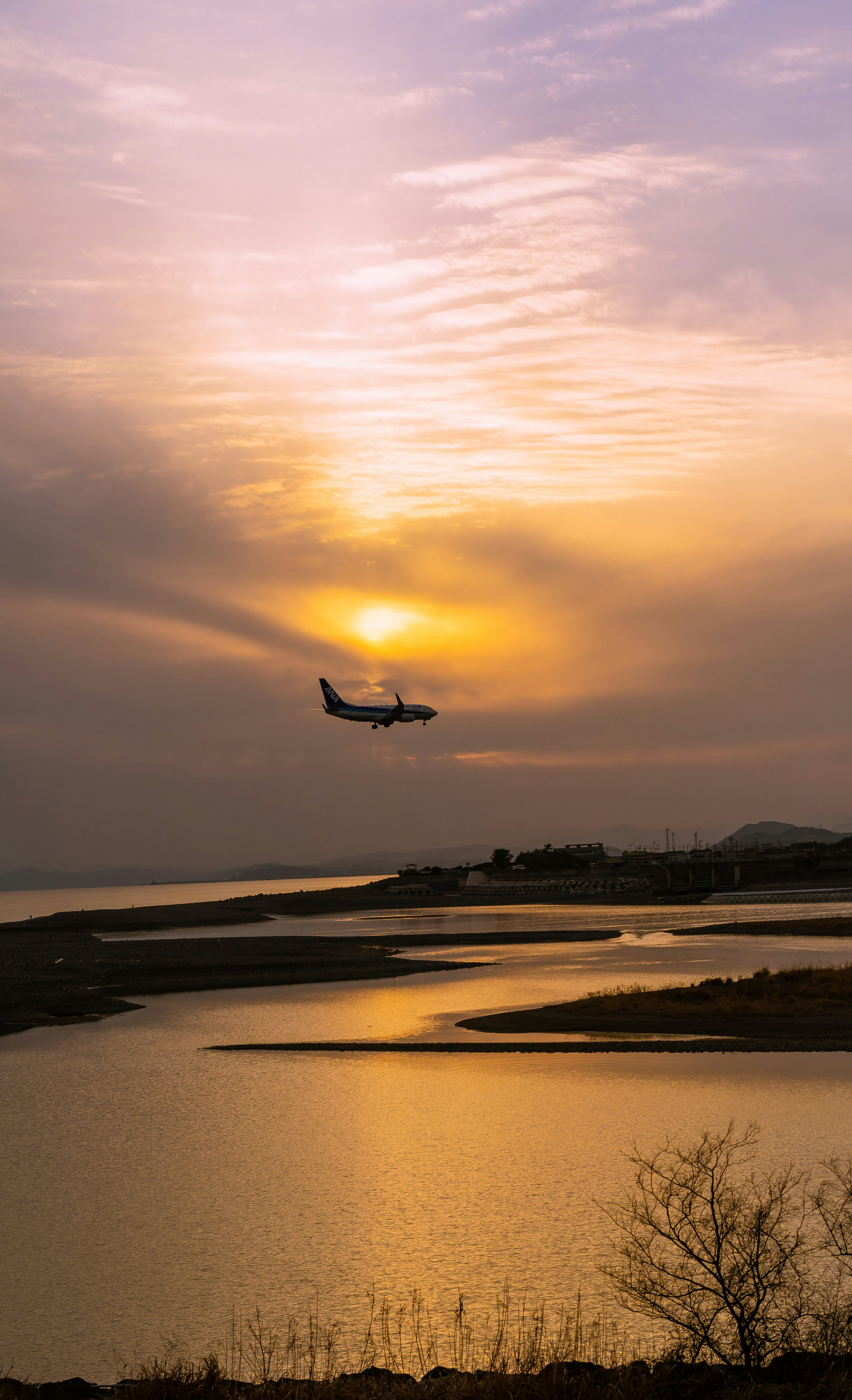 夕焼け空の下を飛ぶ小さな飛行機と川沿いの風景