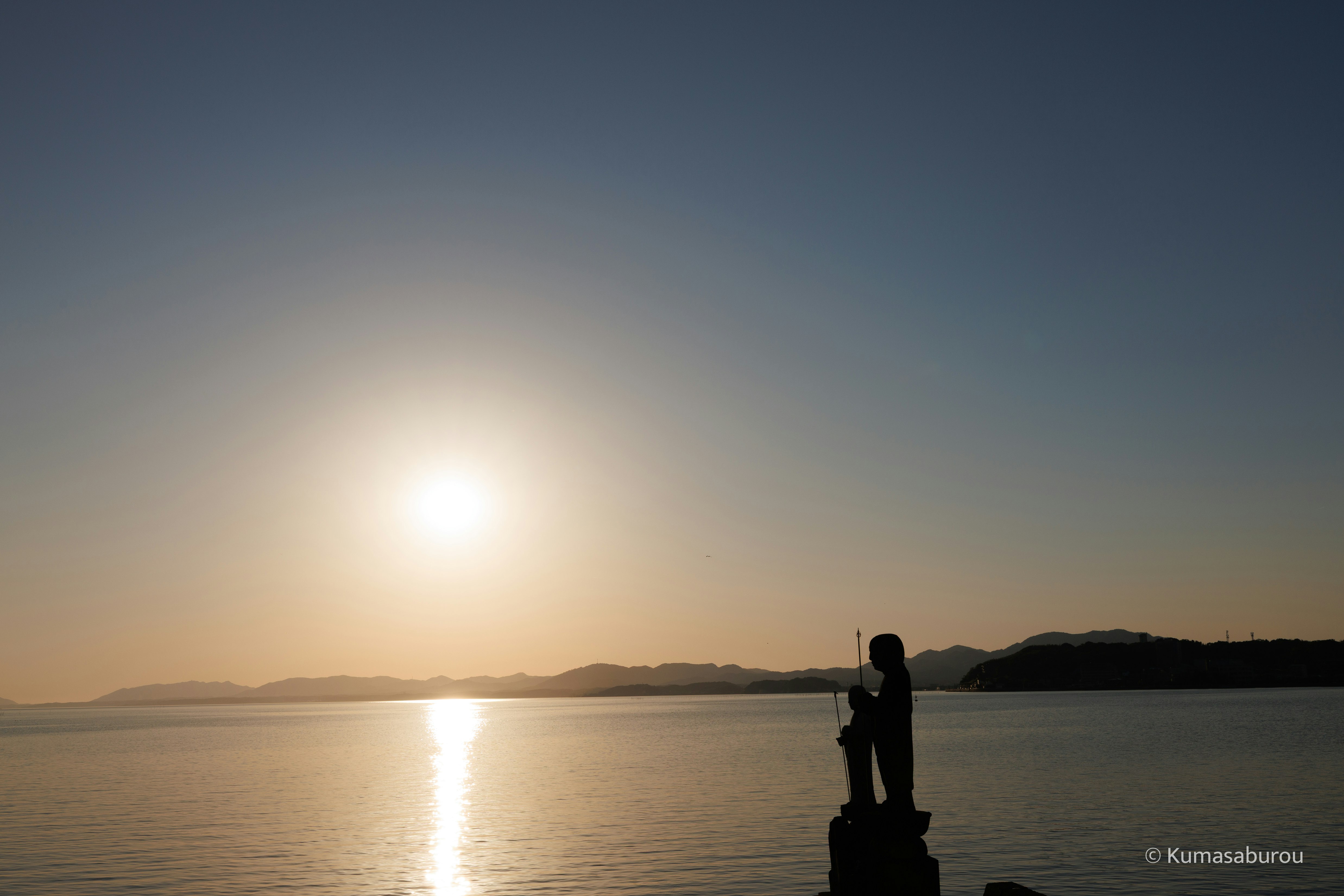 夕日に照らされる湖畔でシルエットの人物が立つ情景